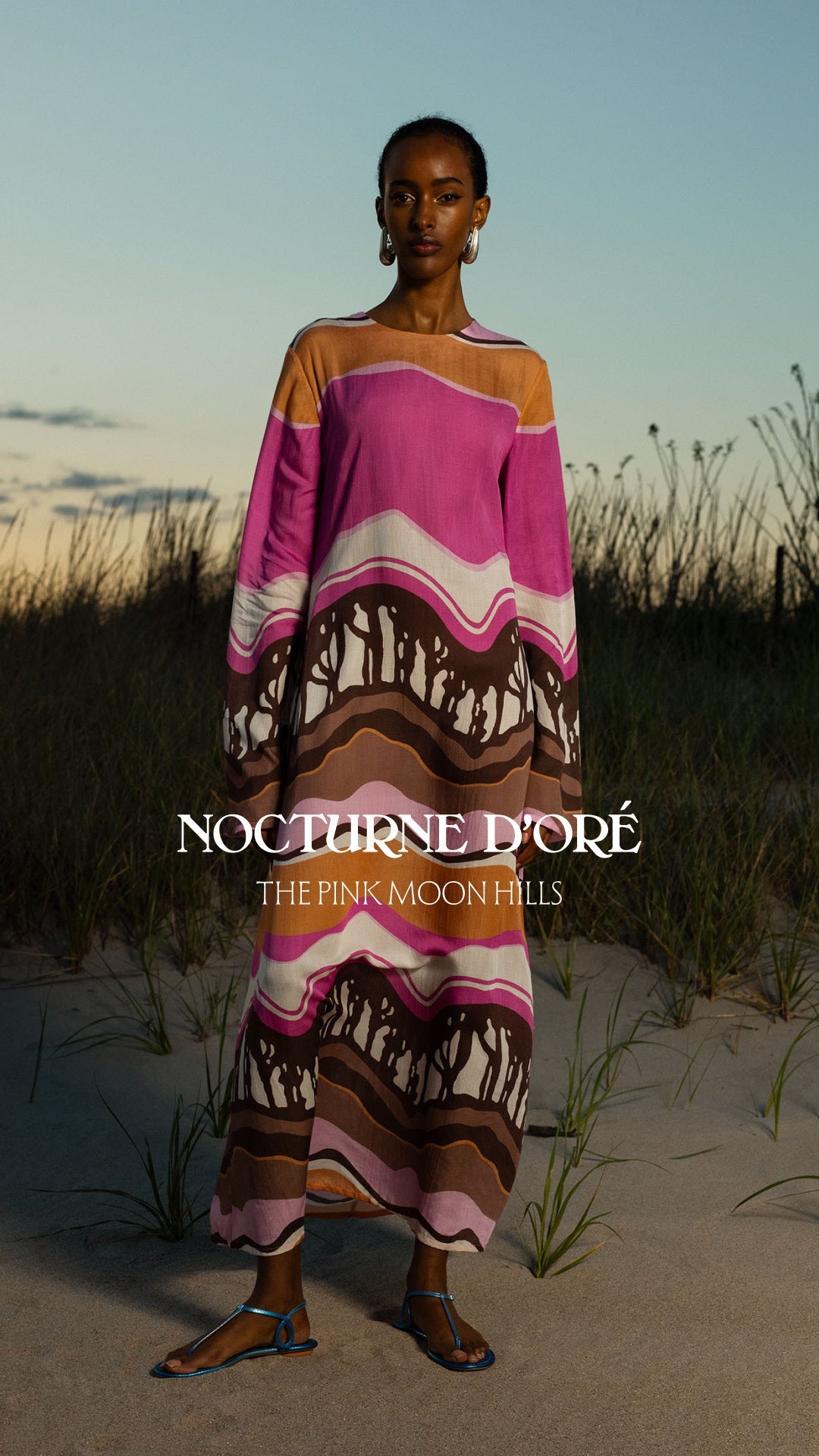 A person wearing a gold and black patterned outfit, sunglasses, and brown boots walks confidently on a sunlit city street against a stone building backdrop.