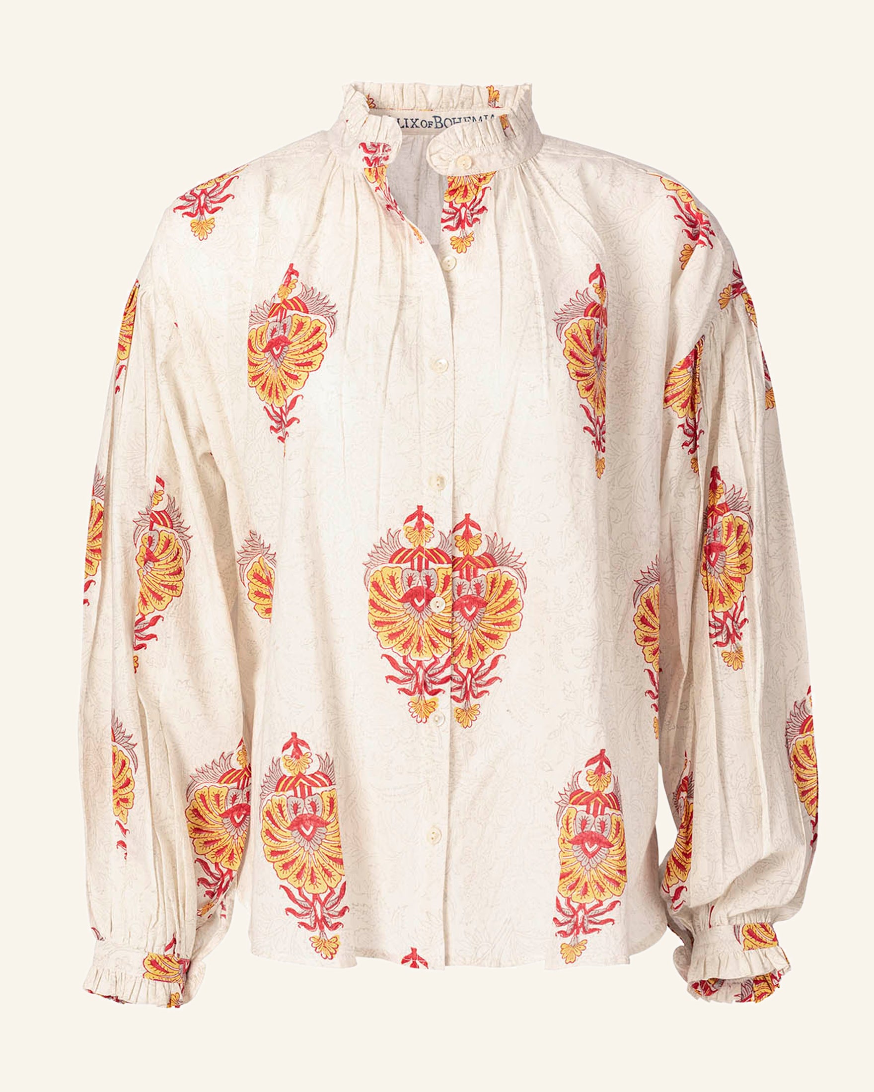 Introducing the Poet Serafina Blouse: a handcrafted white blouse adorned with a vibrant paisley pattern in shades of red, yellow, and orange. Fashioned from cotton using traditional printing techniques, it features long sleeves, a button-up front, a high ruffled collar, and gathered details on the shoulders and cuffs.