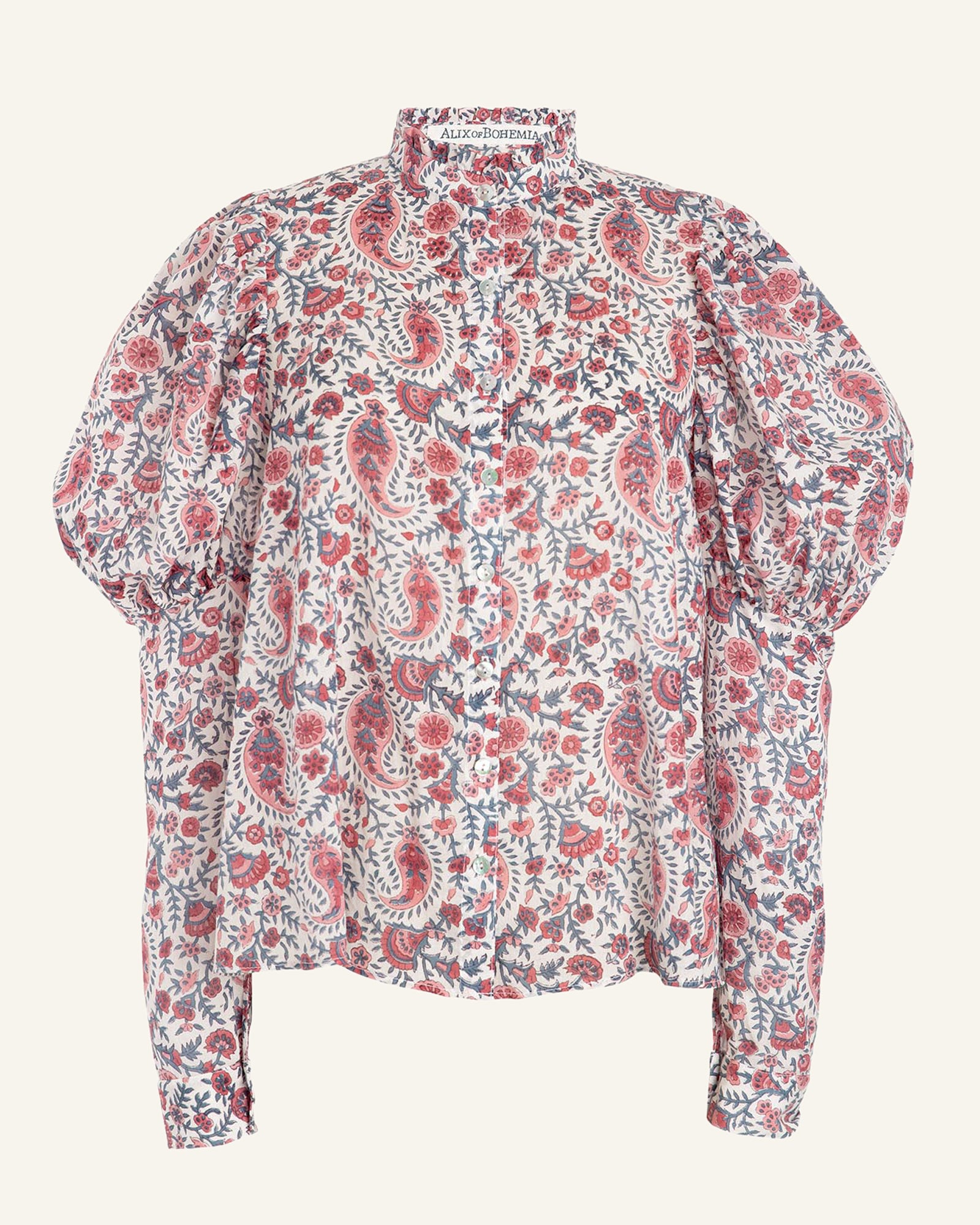 Introducing the Millie Provence Blouse: a long-sleeved, floral piece showcasing a ruffled high neckline. Its fabric boasts a detailed paisley pattern in red, pink, and green against a light backdrop. This hand-block printed blouse is infused with unique charm through its artistic touch and intricate design.