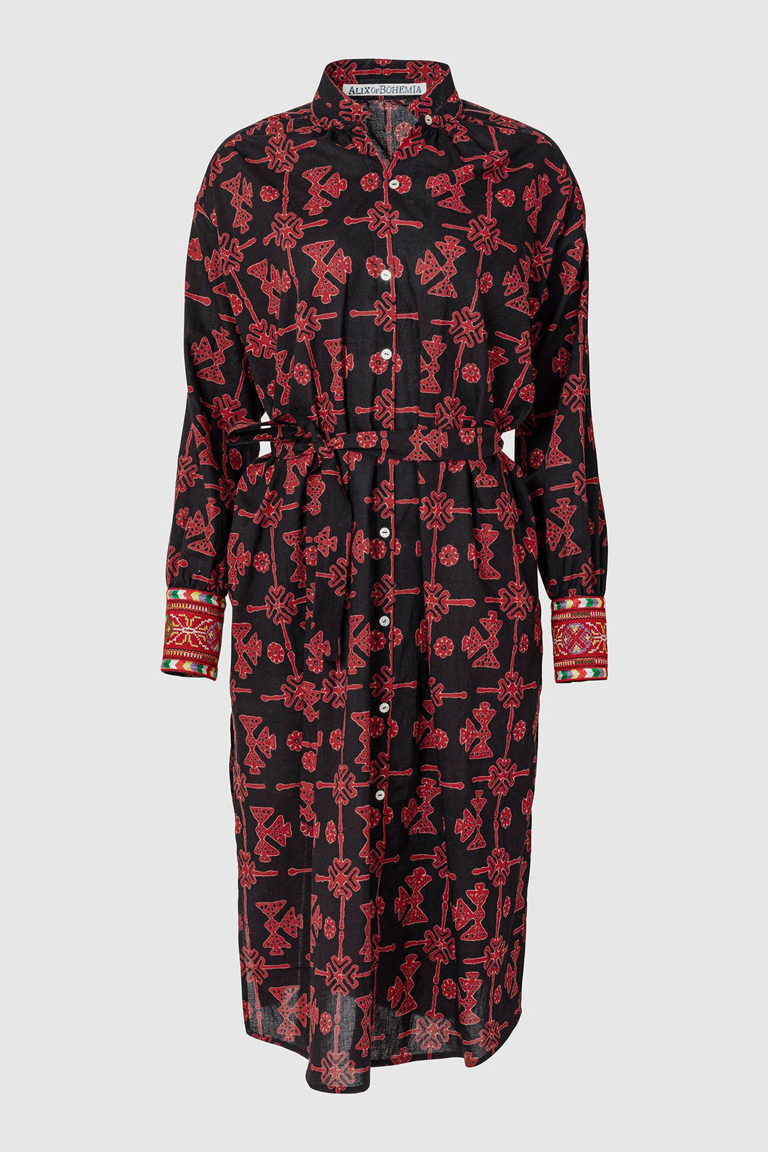 The Shawna Lamu Dress is a long-sleeve shirt dress in black with red geometric and floral patterns. It showcases a button-down front, embroidered cuffs, and a belted waist for a fitted appearance.