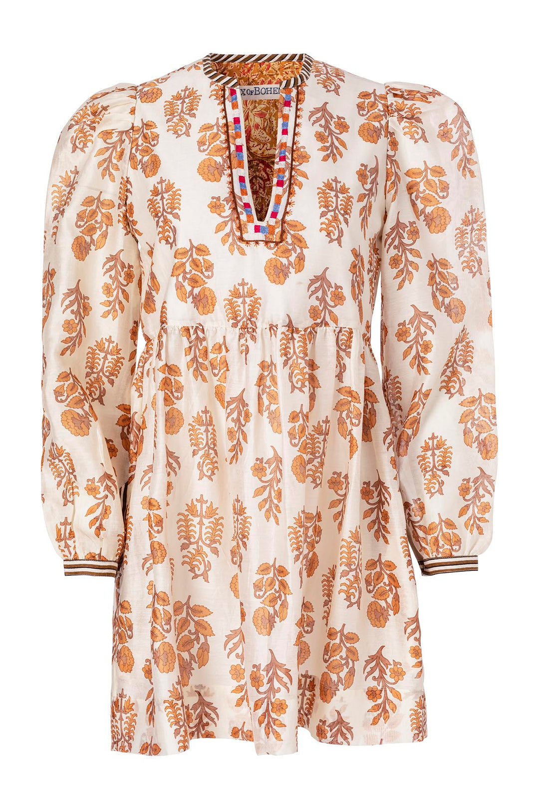 The Whilemina Tumbleweed Dress is a cream-colored garment made from silk cotton, showcasing a floral pattern in hues of brown and rust. It features puffed sleeves, a gathered waist, and a deep V-neckline with hand-embroidered edges crafted using traditional techniques.