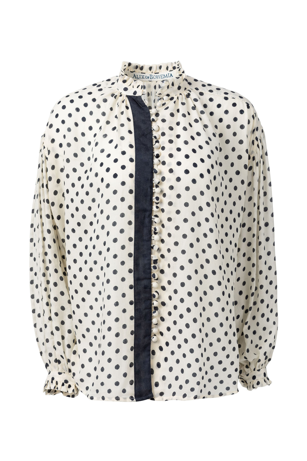 The Prima Tuxedo Spot Blouse is a hand-printed white blouse with black polka dots, featuring a high collar and long sleeves. Made from Cotton Tencel, it includes a black vertical stripe down the front with ruffled edging that adds a stylish contrast to its design.