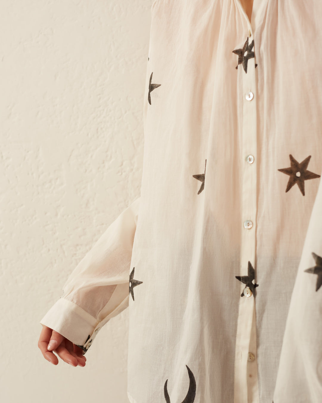 A person wearing the Kiki Stargazer Blouse, featuring a star pattern and Mother of Pearl buttons, stands against a textured white wall.