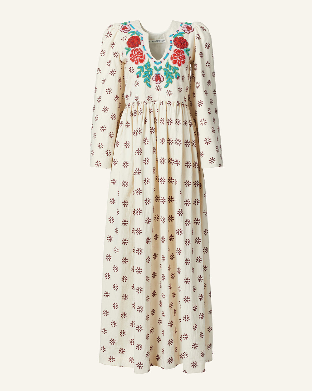 The Clementine Rambling Rose Dress is a luxurious cream, long-sleeved dress made from silk. It boasts a delicate pattern of small red flowers and features a v-neckline adorned with large, hand-embroidered floral designs, including vibrant red roses and green leaves. The gathered waist enhances its flowing silhouette.