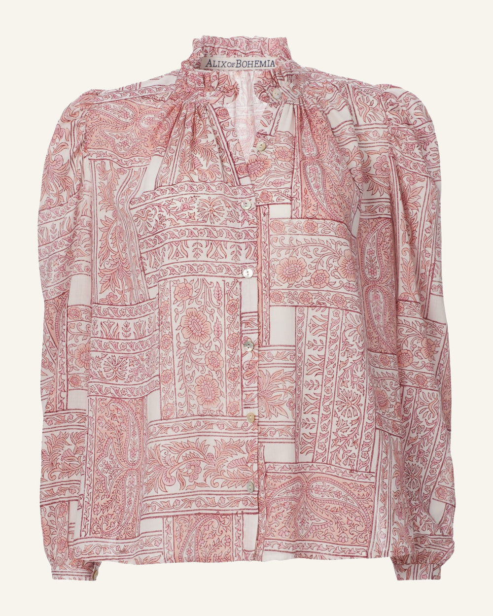 The Annabel Pink Crossroad Shirt is a long-sleeved blouse crafted from hand-printed Tencel, featuring an intricate red and white paisley patchwork. It includes a high ruffled collar and a button-down front, enhancing its elegant design.