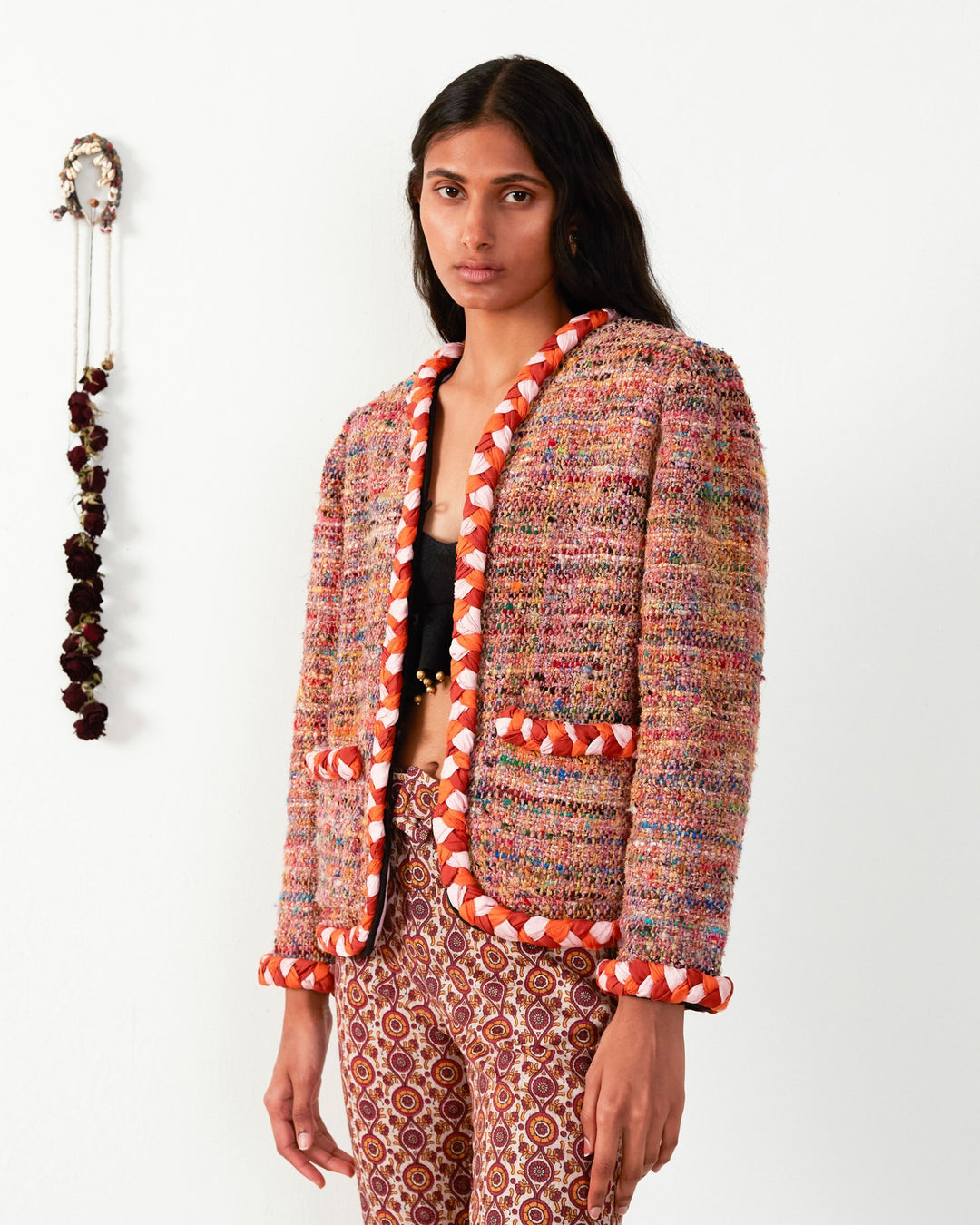 A person stands before a white backdrop, wearing the Billie Rose Dust Bouclé Jacket made from recycled fibers, featuring vibrant colors with red and white trim.