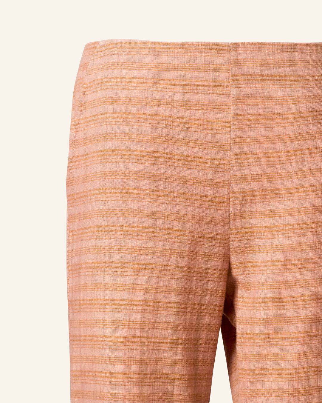 A close-up of the Charlie Juted Rose Pant, featuring a light orange color with a subtle plaid pattern and a hand-stitched hem, shown from the back against a plain off-white background.