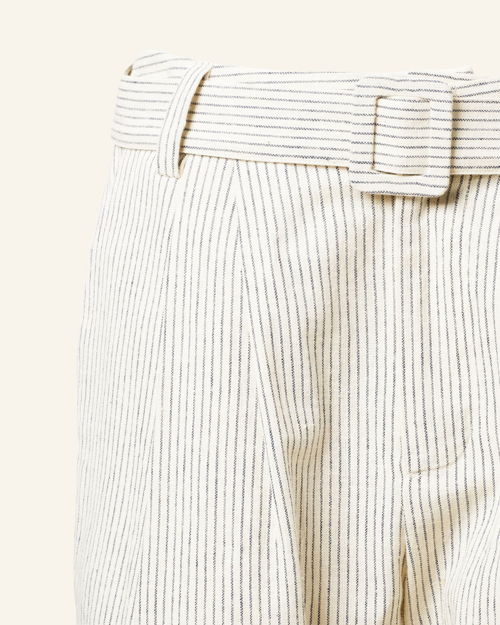 Close-up of the Colette Cloud Stripe Belted Pant, featuring a high-waisted design with a matching belt and buckle. The beige fabric is adorned with vertical thin dark lines, offering a sophisticated and classic design that evokes traditional ikat patterns.