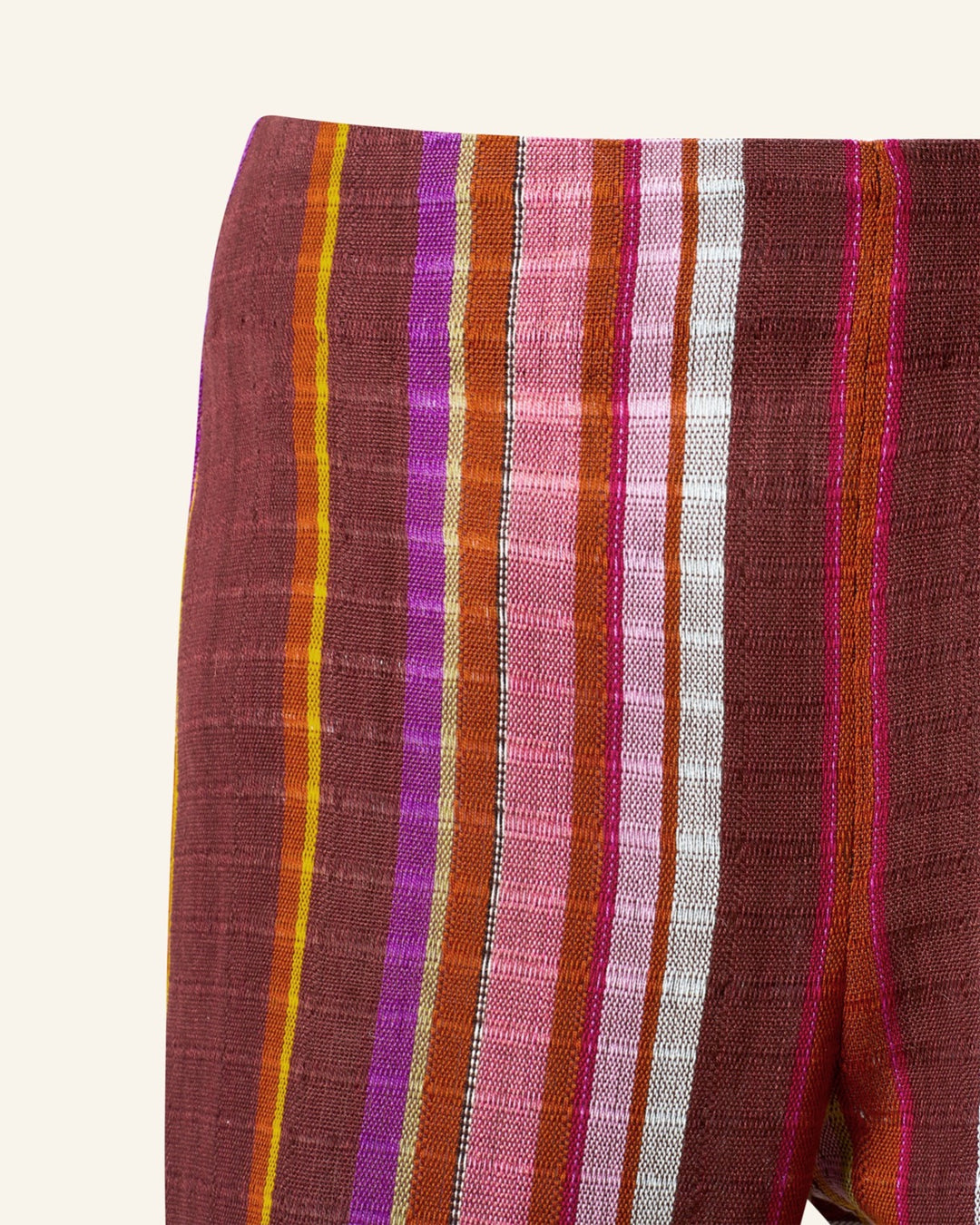 Close-up of the Farah Berry Truffle Flare Pant featuring vertical stripes in pink, orange, red, and white on a brown background. The textured fabric captures the vibrant essence of Guatemalan ikat weaving.