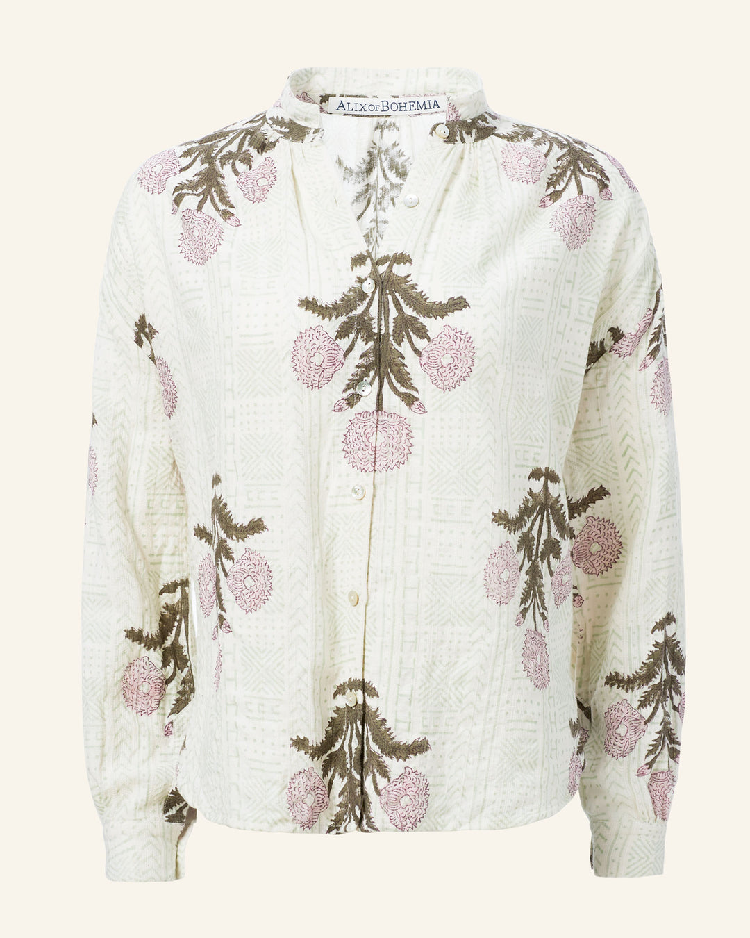 The Kiki Blush Triple Bloom Shirt is a long-sleeved blouse adorned with a floral pattern in pink and green on a light cream background. Made from hand-loomed cotton, it features large flowers and branches, along with a mandarin collar and button-down front.