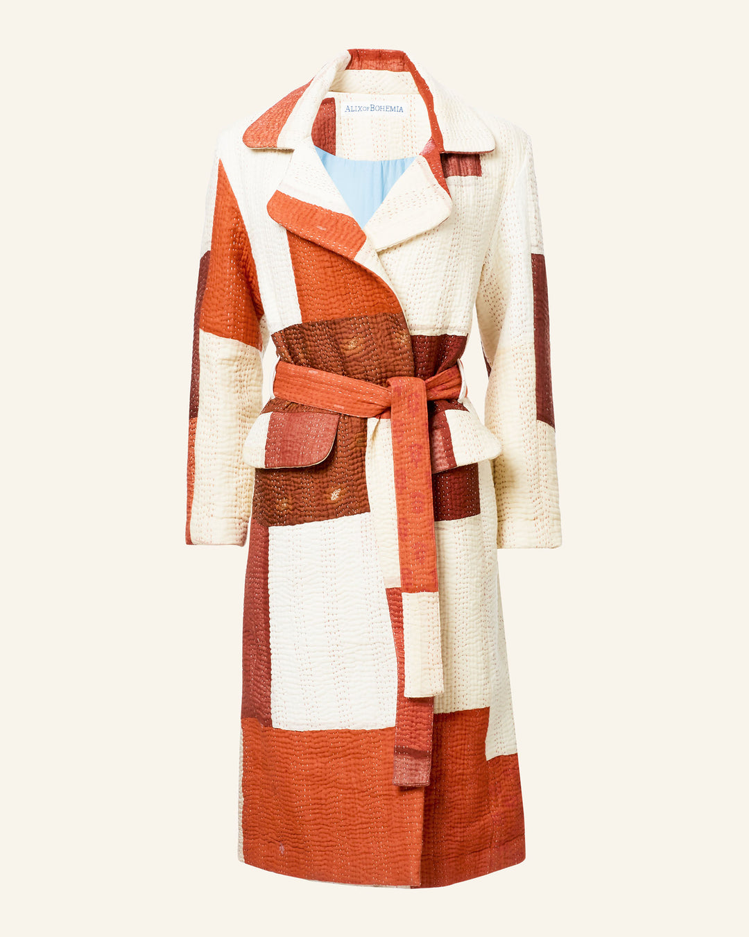 The Officer Almond Kantha Coat is a long, belted coat with a patchwork design in white, red, and brown shades made from recycled silk and showcased on a plain background.