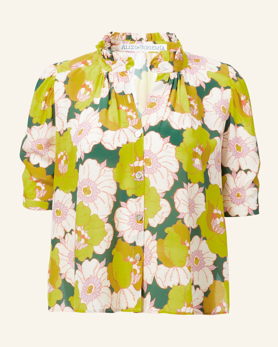 Winnie Citrus Blossom Silk Shirt, featuring a ruffled collar and short sleeves, displays large pink flowers and green leaves against a lush green background.