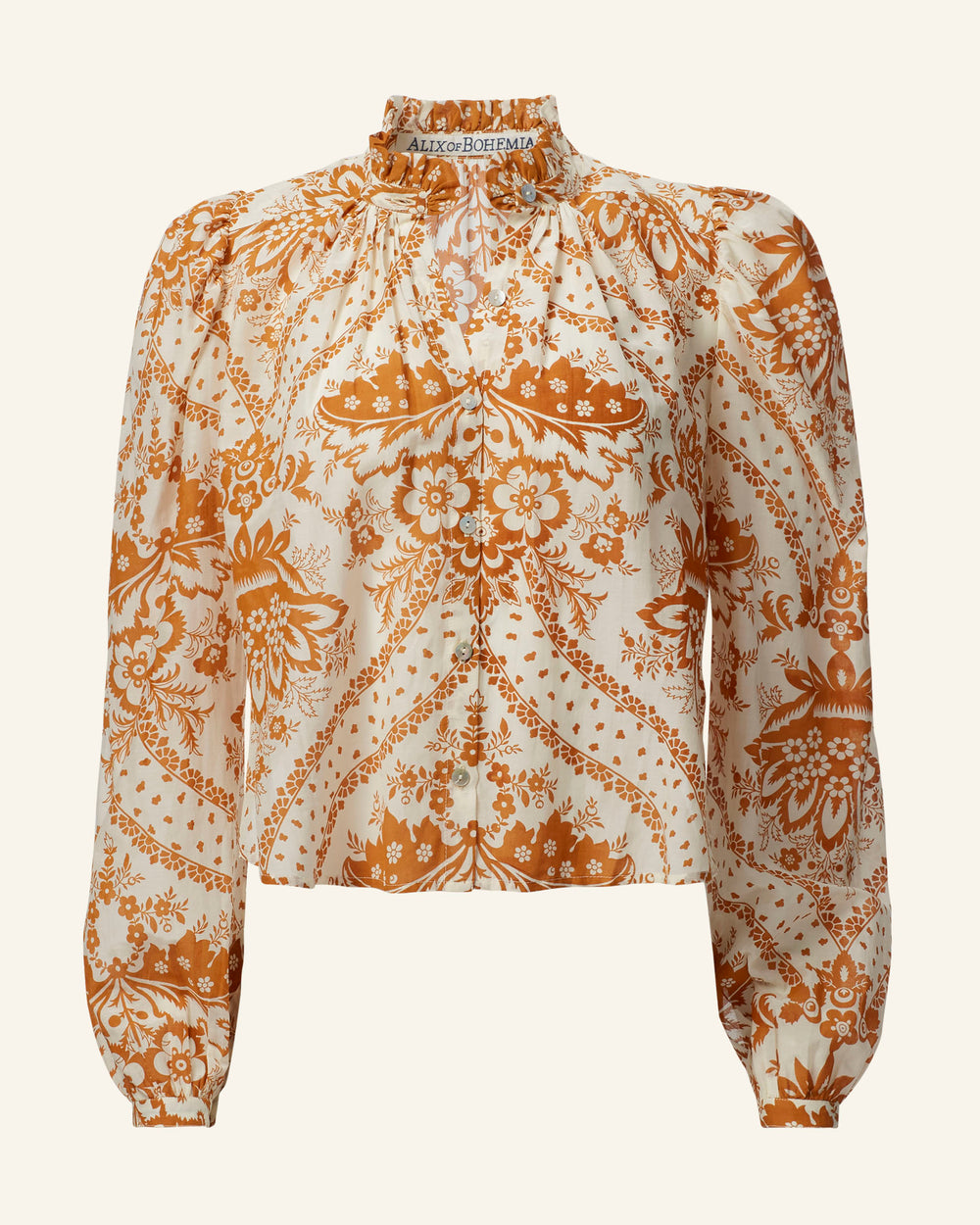 The Annabel Sunglow Shirt is a long-sleeve blouse featuring a high ruffled collar and an intricate orange floral motif intertwined with a paisley pattern on a white background. Crafted from lightweight fabric, this vintage-inspired shirt is adorned with charming button details down the front, exuding timeless elegance.