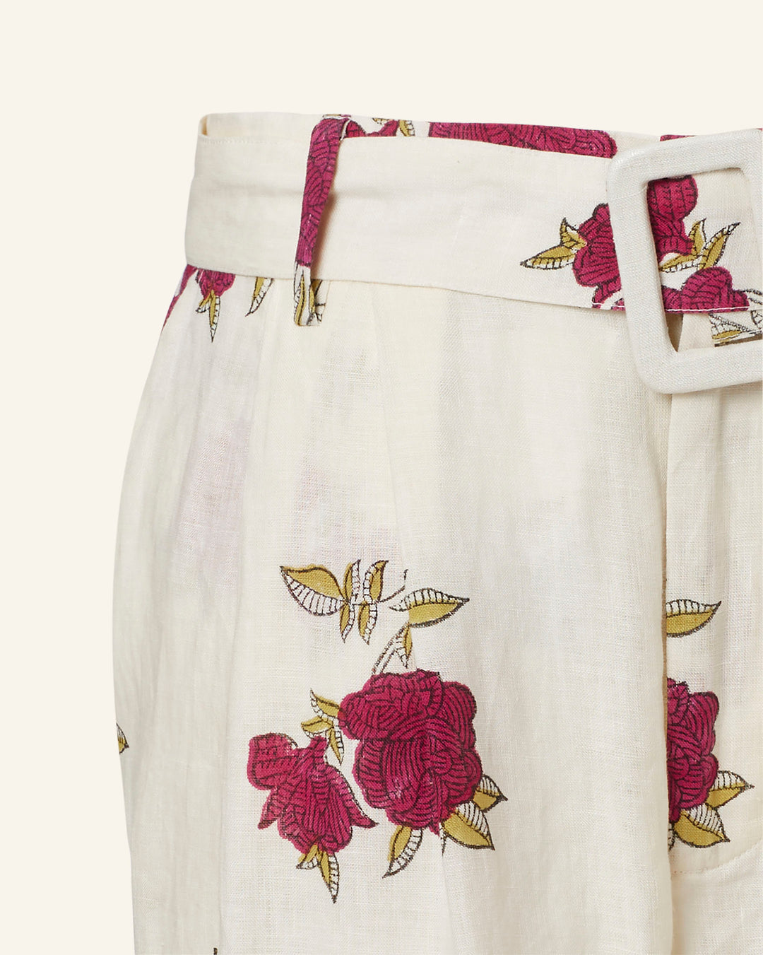 Close-up of the Colette Cerise Rosette Pant, showcasing its cream-colored high-waisted design adorned with red floral patterns and pink rose print. It features a matching fabric belt with a square buckle and includes hand-printed leaves accented in yellow alongside the flowers.