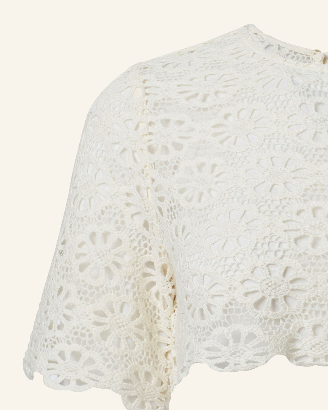 Close-up of the Nala Daisy Lace Cropped Top, a cream-colored crocheted piece featuring a delicate daisy motif. This intricate cotton lace design showcases circular flowers with a scalloped edge against a light neutral background.