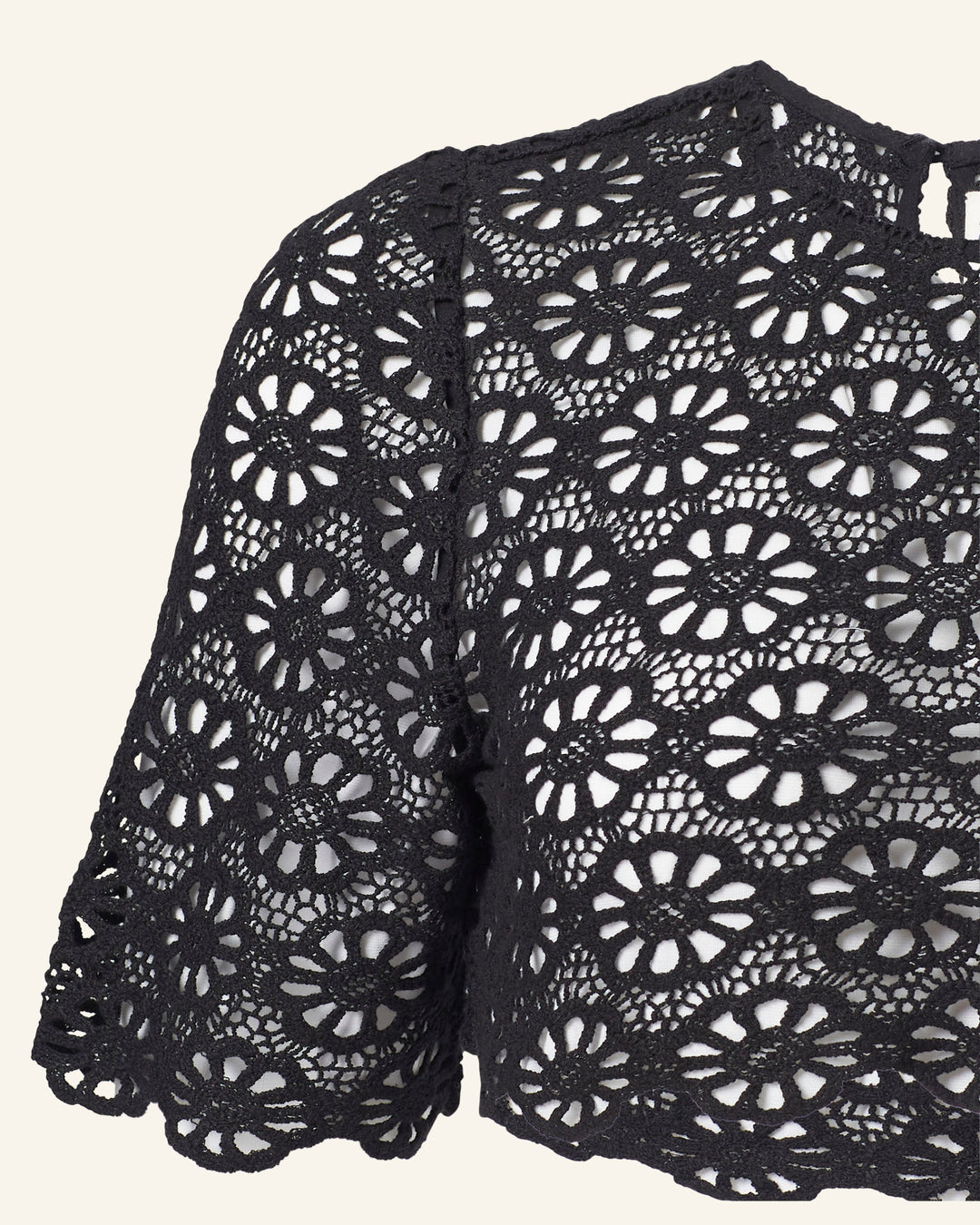 A close-up of the Nala Onyx Lace Cropped Top, intricately fashioned with circular daisy motifs and scalloped edges. This black lace top offers a delicate contrast, showcasing a light background through its detailed design.