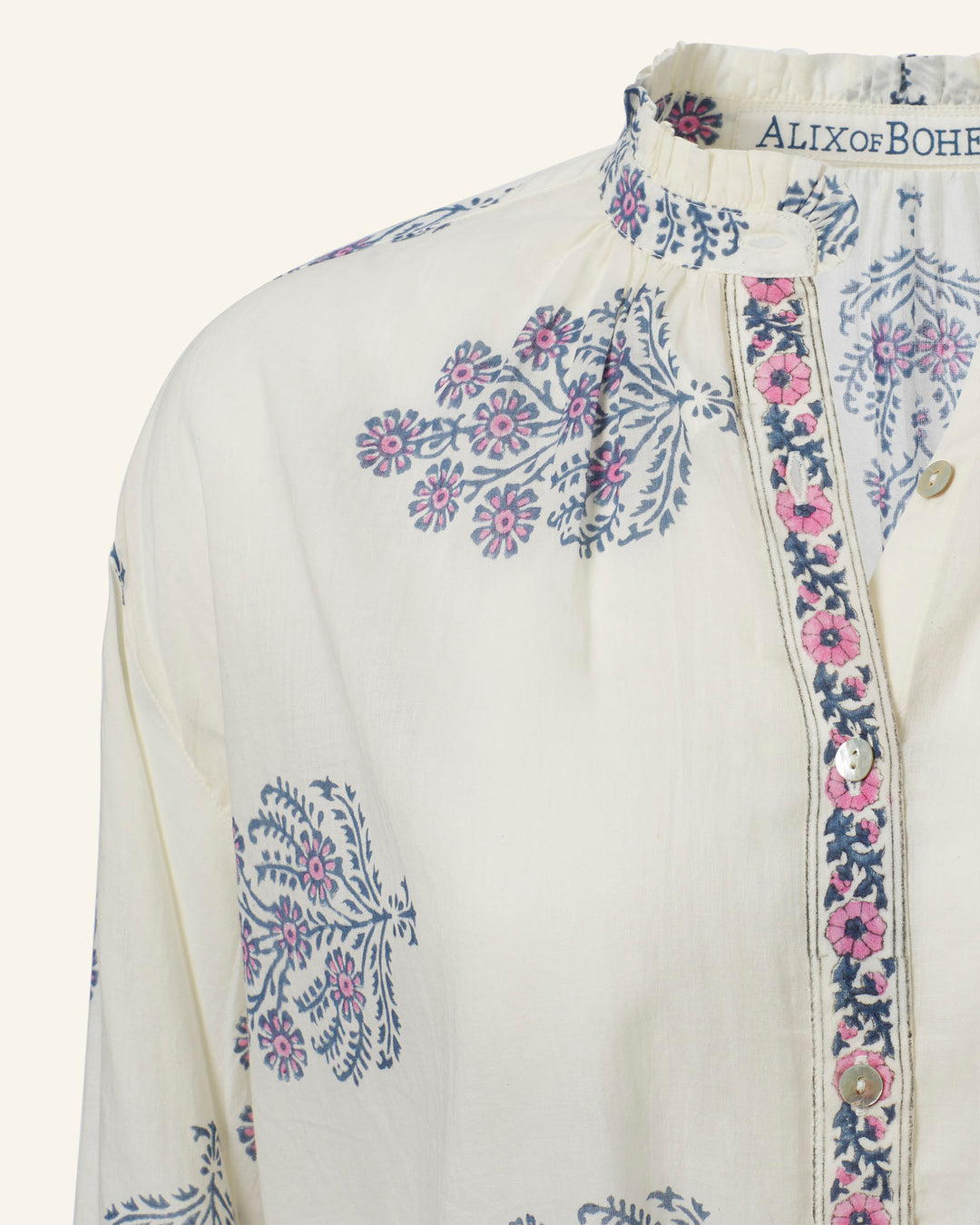 The image showcases a detailed view of the Poet Freesia Phlox Blouse, adorned with a light-colored floral print featuring blue and pink patterns. The blouse is distinguished by its high collar with embroidered accents and small round buttons down the front, reminiscent of a vintage-inspired folk shirt. The label indicates it is by "ALIX of BOHEMIA.