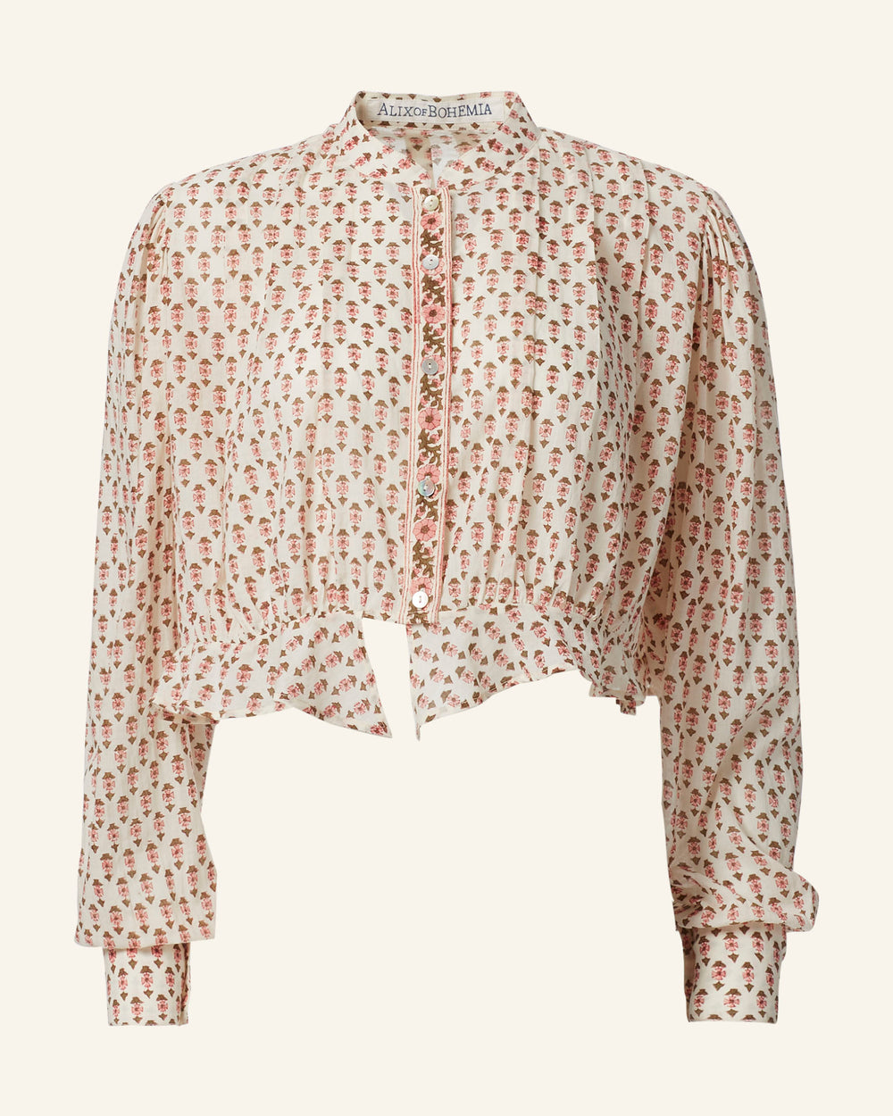 The Ryland Ruby Quatrefoil Top, a white cropped blouse made from cotton voile, features a Victorian silhouette with its button-down front, high collar, and cuffed sleeves adorned with a floral print.