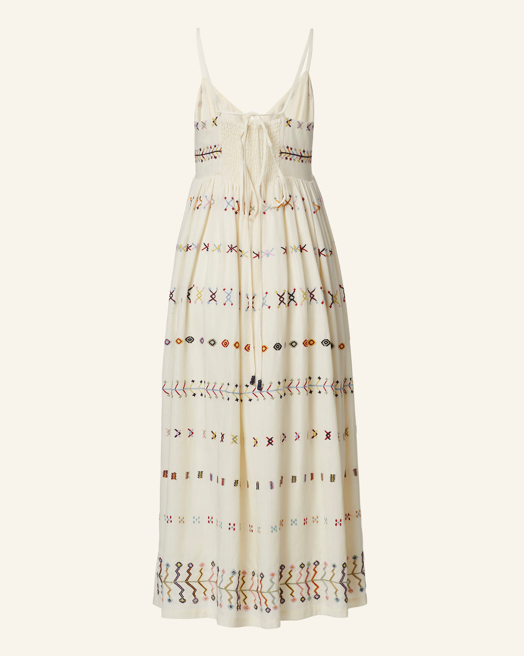 The Skylar Aurora Arrow Dress is a white, ivory sleeveless maxi dress with thin straps and a smocked bodice. This hand-embroidered summer dress showcases multicolored geometric patterns in horizontal rows, creating an intricate and vibrant design that exudes bohemian elegance.