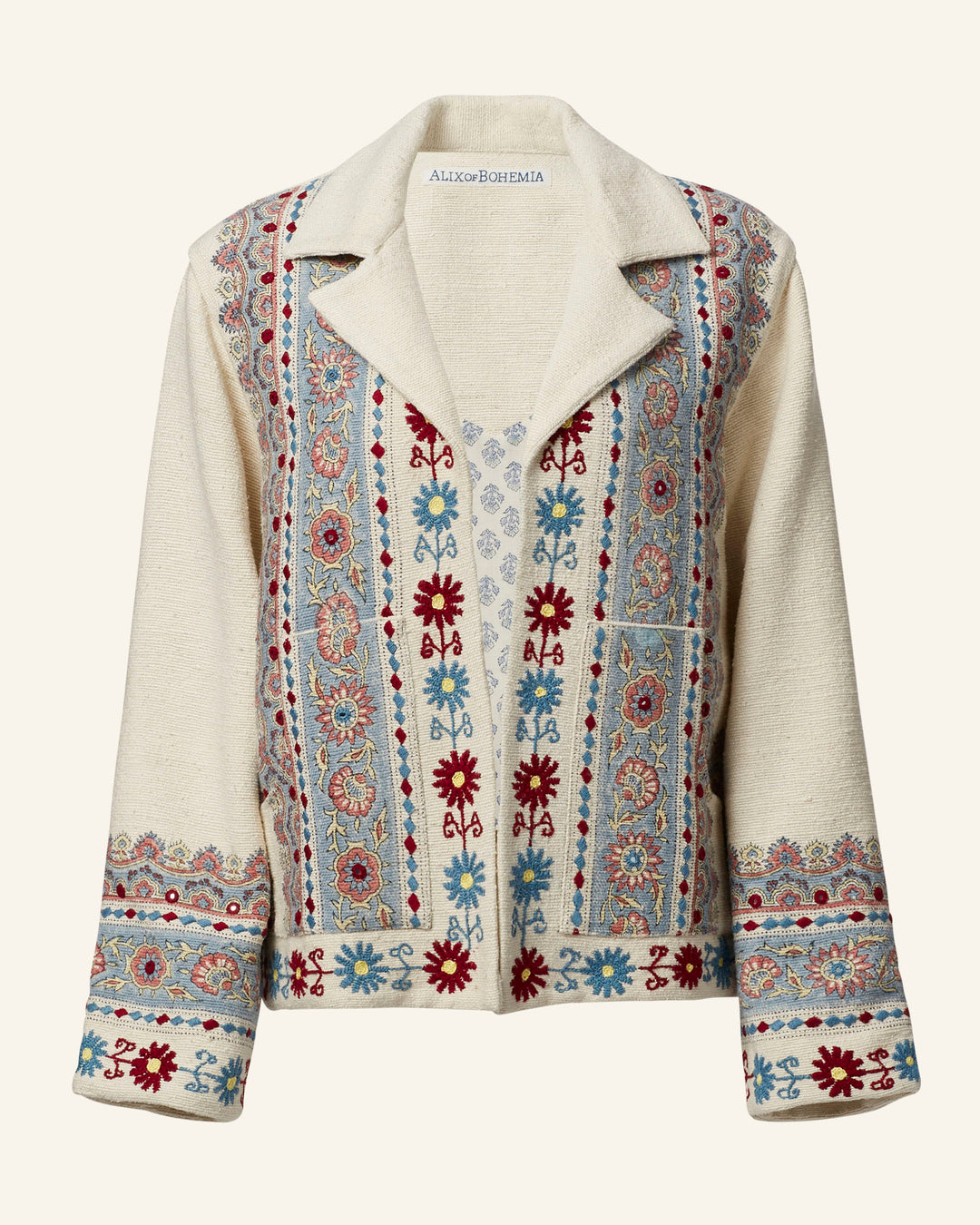 Introducing the Western Riviera Silk Jacket: A stunning cream-colored piece featuring intricate hand embroidery with red and blue floral patterns intertwined with geometric designs. It highlights a wide collar and long sleeves with beautifully detailed cuffs, capturing a bohemian essence. This statement jacket is ideal for anyone looking to add a unique flair to their wardrobe.