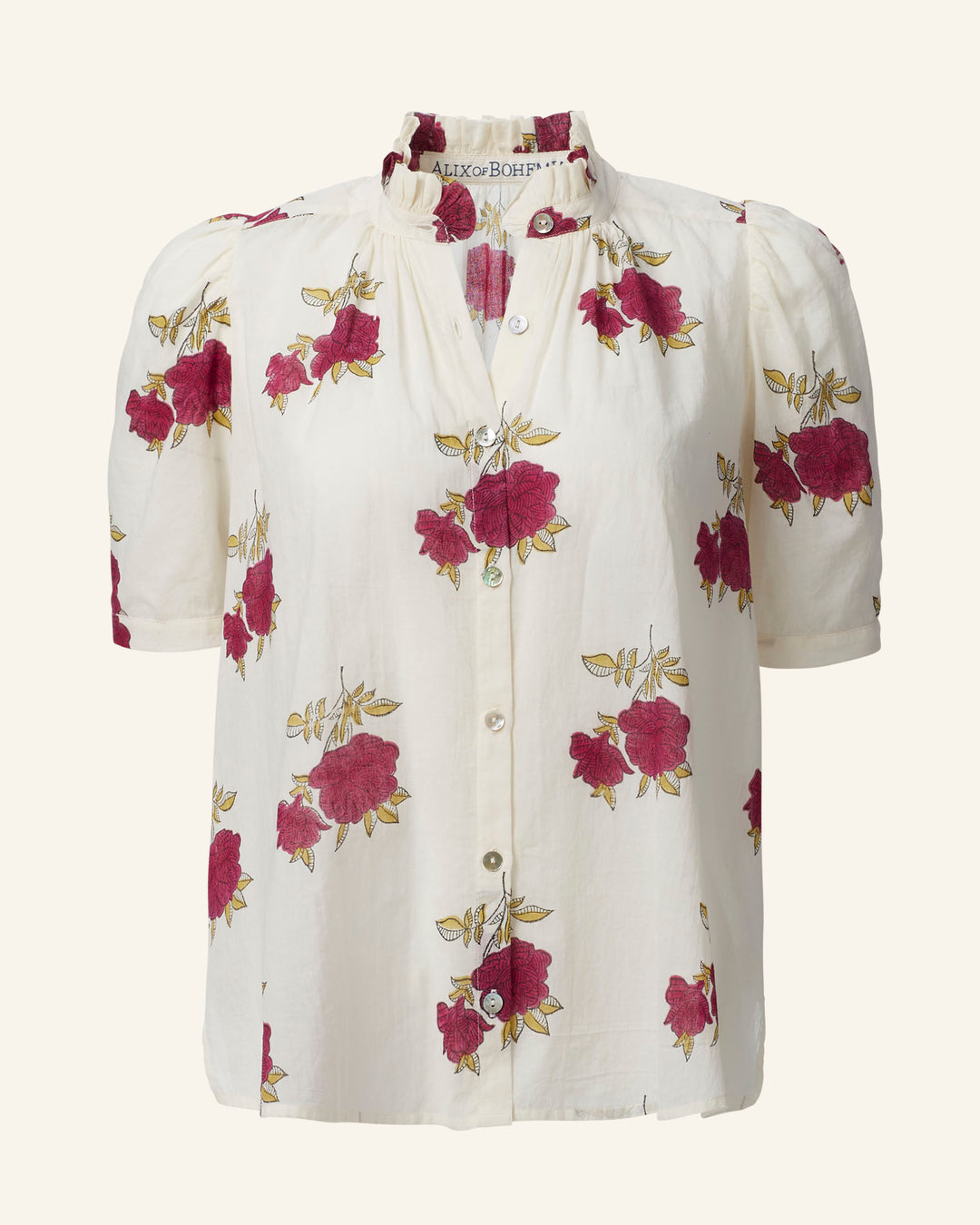 The Winnie Cerise Rosette Shirt is a cream-colored blouse made from cotton voile, adorned with a charming rose motif that includes pink and red roses surrounded by green leaves. This hand-block printed piece features short puff sleeves, front buttons, and a delicately ruffled neckline for an elegant touch.