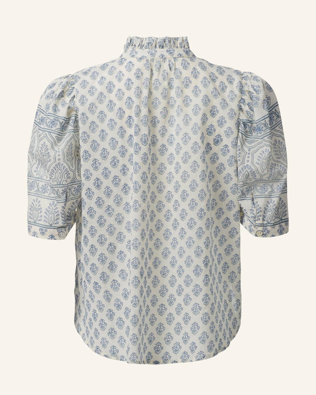 The Winnie Delft Bhutti Shirt is a vintage-inspired blouse made from cotton voile, showcasing blue floral and paisley patterns. It has a high ruffled collar, puffed short sleeves, and offers a relaxed fit. The detailed design enhances the simple silhouette with elegance.