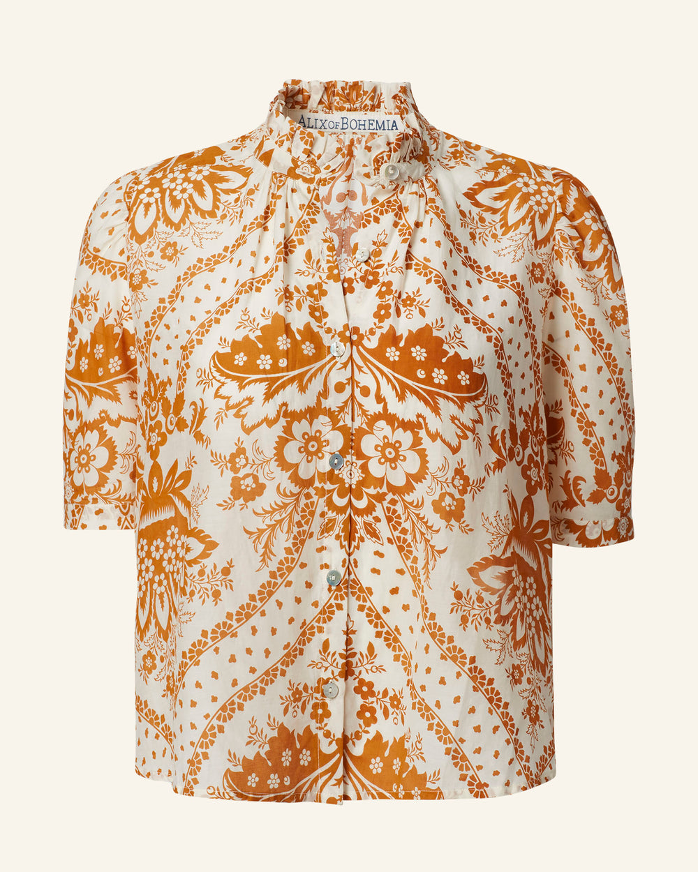 The Winnie Sunglow Shirt is a vintage-inspired button-up blouse featuring an intricate orange floral motif and paisley pattern on a cream background. It has a high neck, short sleeves, and elegant mother-of-pearl buttons down the front. The fabric boasts a light, textured appearance.