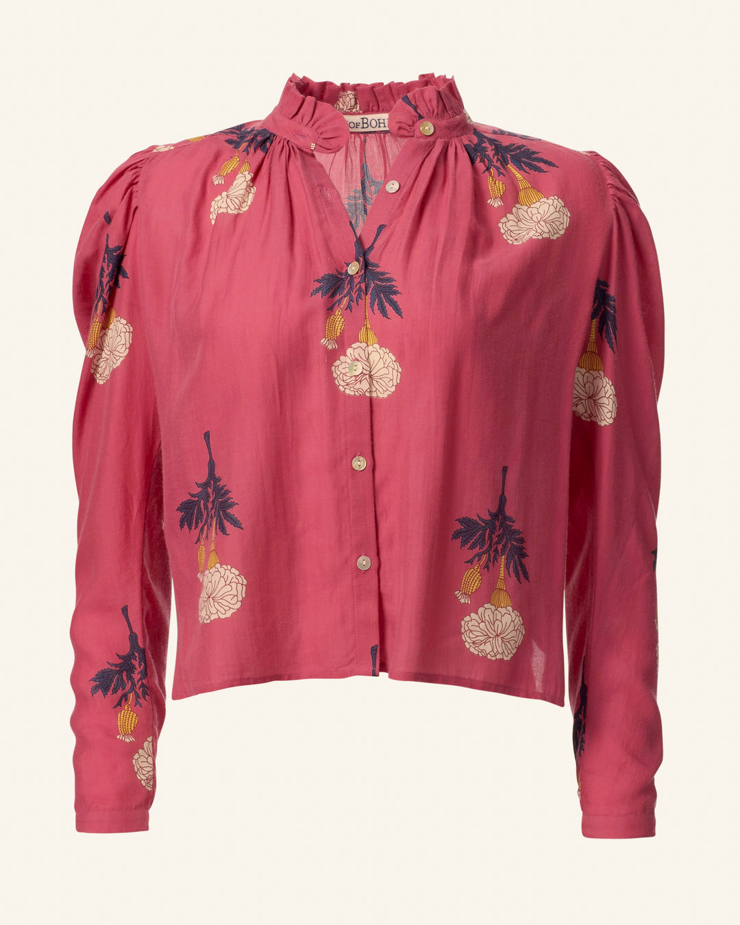 The Arte Hibiscus Rose Shirt is a long-sleeved blouse with a vintage feel, showcasing deep pink tones adorned with floral patterns. It features cream and dark blue hand-embroidered flowers, complemented by a ruffled neckline and slightly puffed shoulders.