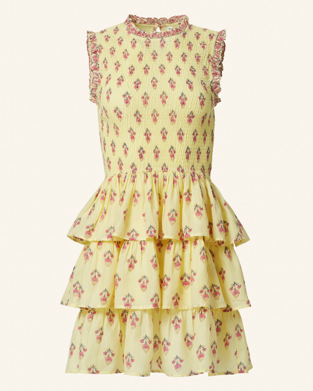 The Caeli Primrose Bhutti Dress is a yellow sleeveless piece with a tiered skirt, featuring pink floral patterns and ruffled edges that evoke a seaside atmosphere.