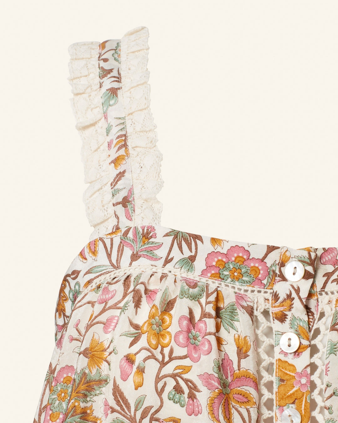 Close-up of the Effie Garden Party Silk Top, featuring a hand-block printed floral pattern with ruffled straps and front buttons. The fabric displays pink, orange, and green flowers with leaves, accented by white lace trim on the straps for a touch of vintage elegance.