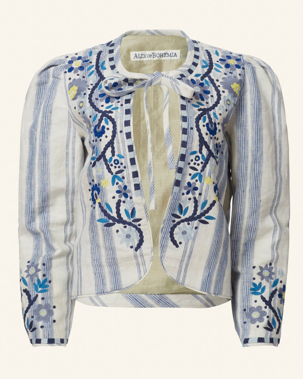 The Fiorello Pacific Reef Jacket is a blue and white striped silk-linen blazer, featuring intricate floral embroidery with a front tie detail. The hand-embellished patterns showcase flowers and leaves in shades of blue and yellow. The label is "Alix of Bohemia.