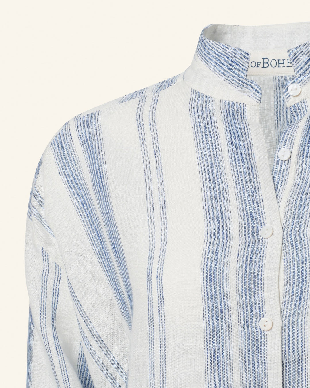 A close-up of the Kiki Pacific Star Shirt reveals its cotton voile fabric adorned with vertical blue stripes and a subtle blue-and-white floral print. The band collar and white buttons along the placket elevate its casual yet stylish look, making it ideal for any laid-back occasion.