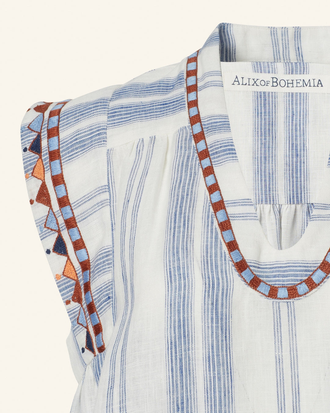 A close-up of the Nehru Pacific Embroidered Top by Alix of Bohemia, a vintage-inspired blue and white striped blouse adorned with intricate embroidery along the neckline and sleeves, showcasing geometric patterns in blue, orange, and red on beautifully textured lightweight fabric.