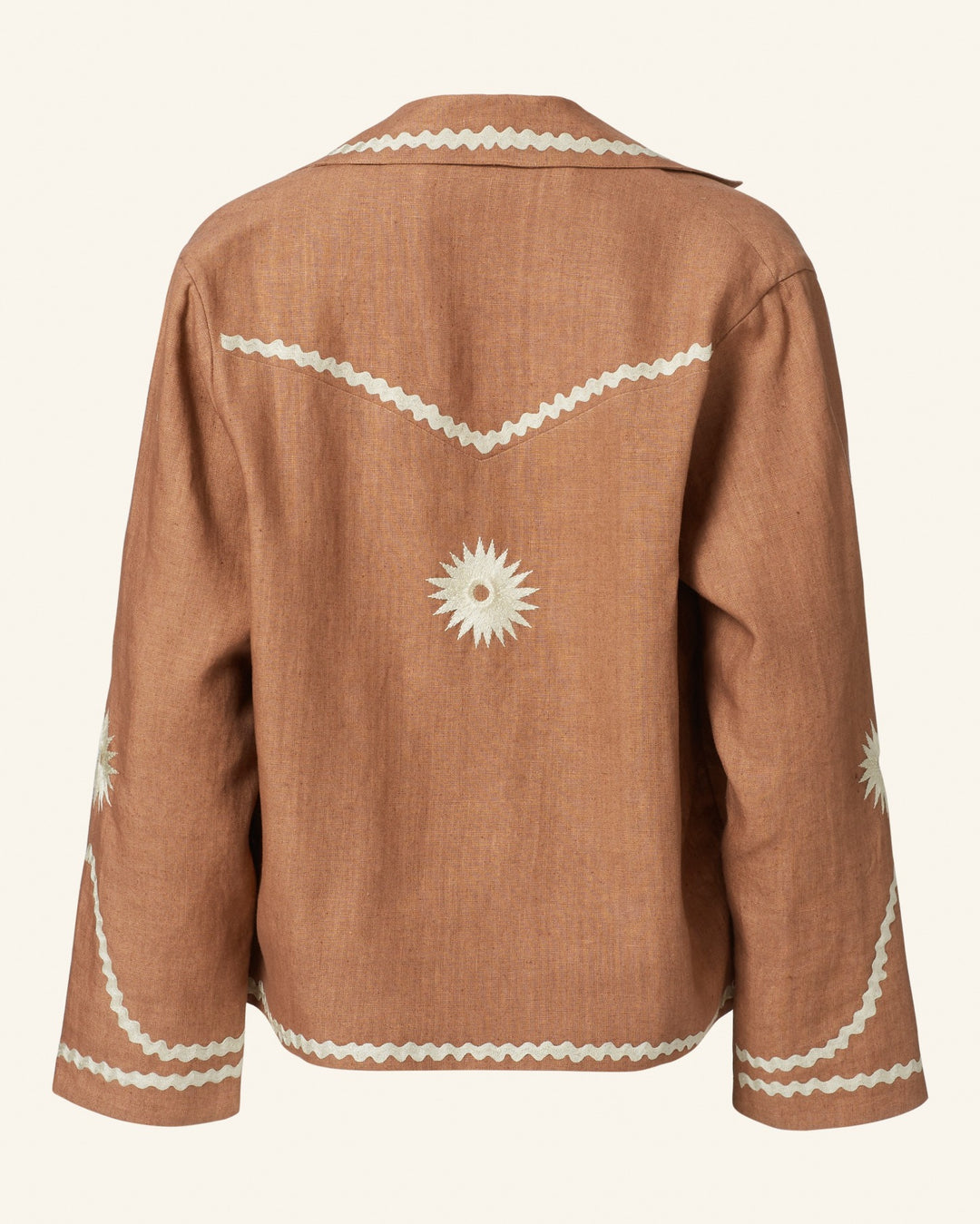 Back view of the Western Clove Ric Rac Jacket in tan, showcasing white zigzag trim and starburst patterns on the back and sleeves, highlighted by mother-of-pearl buttons for an elegant touch. This jacket offers a casual, relaxed fit with retro charm that pairs perfectly with the Charlie Deep Sea Daisy Pant.