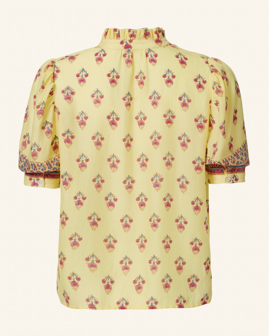 Discover the Winn Primrose Bhutti Shirt, a vintage-inspired cotton voile blouse in vibrant yellow. It showcases an enchanting floral motif with red and pink flowers and features short, puffed sleeves adorned with decorative buttons. The high neck is elegantly highlighted by subtle ruffles, while the back is enhanced with a stylish pleat for added detail.