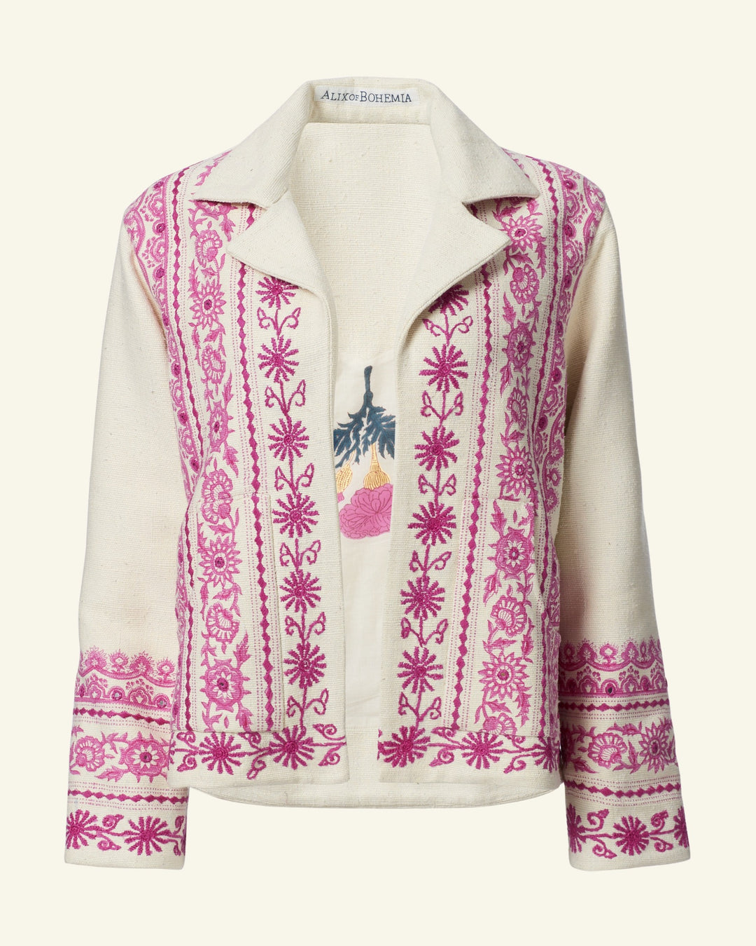 The Western Phlox Riviera Jacket features a cream-colored linen design with hand-embroidered pink floral patterns on the front and sleeves. It has a stylish collar and an open front, allowing a peek at the shirt underneath that showcases leaves and a pink flower. This jacket is an ideal choice for summer wear.