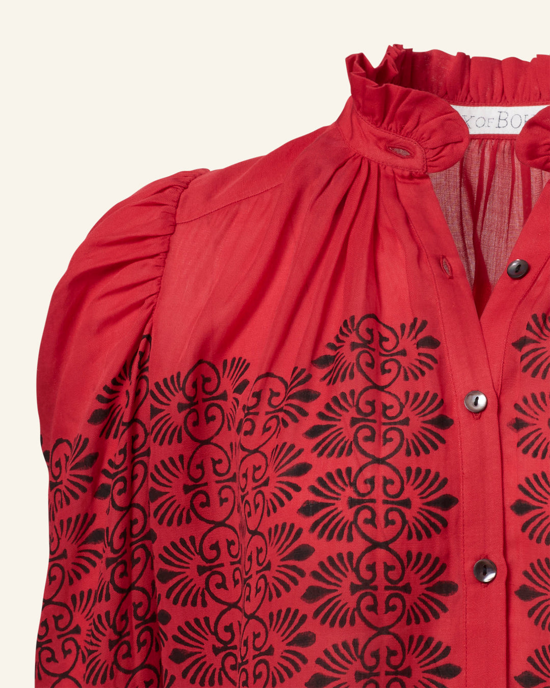 The Artemis Cherry Trellis Shirt, adorned with black intricate floral embroidery on a red background, exudes a vintage-inspired charm. It features a high, ruffled neckline, gathered shoulders, and a button-down front that provides a lightweight and slightly sheer feel.