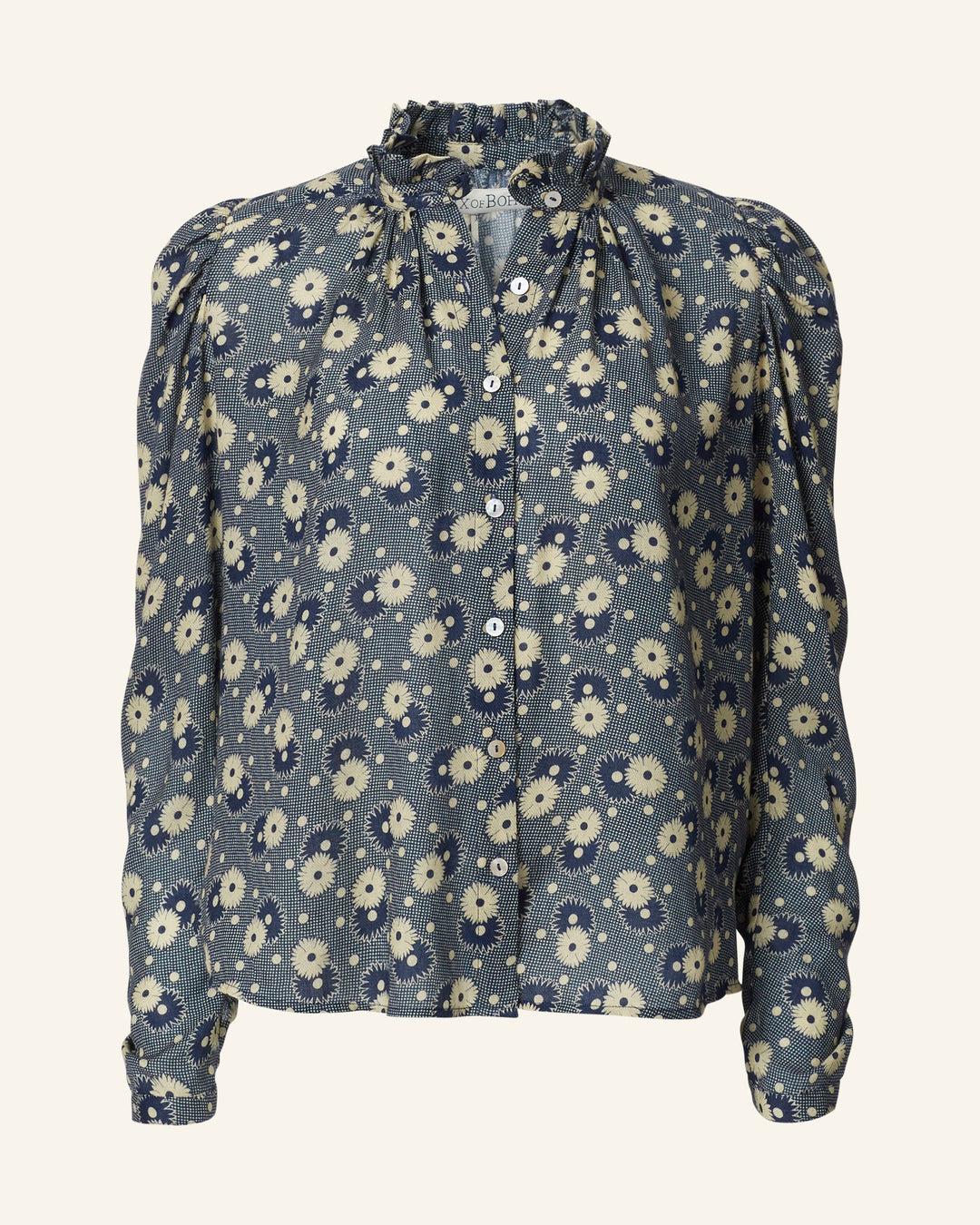 A long-sleeved, button-up blouse with a ruffled collar, showcasing a navy background adorned with a '70s-style daisy print of petite white flowers, known as the Artemis Navy Daisy Shirt.