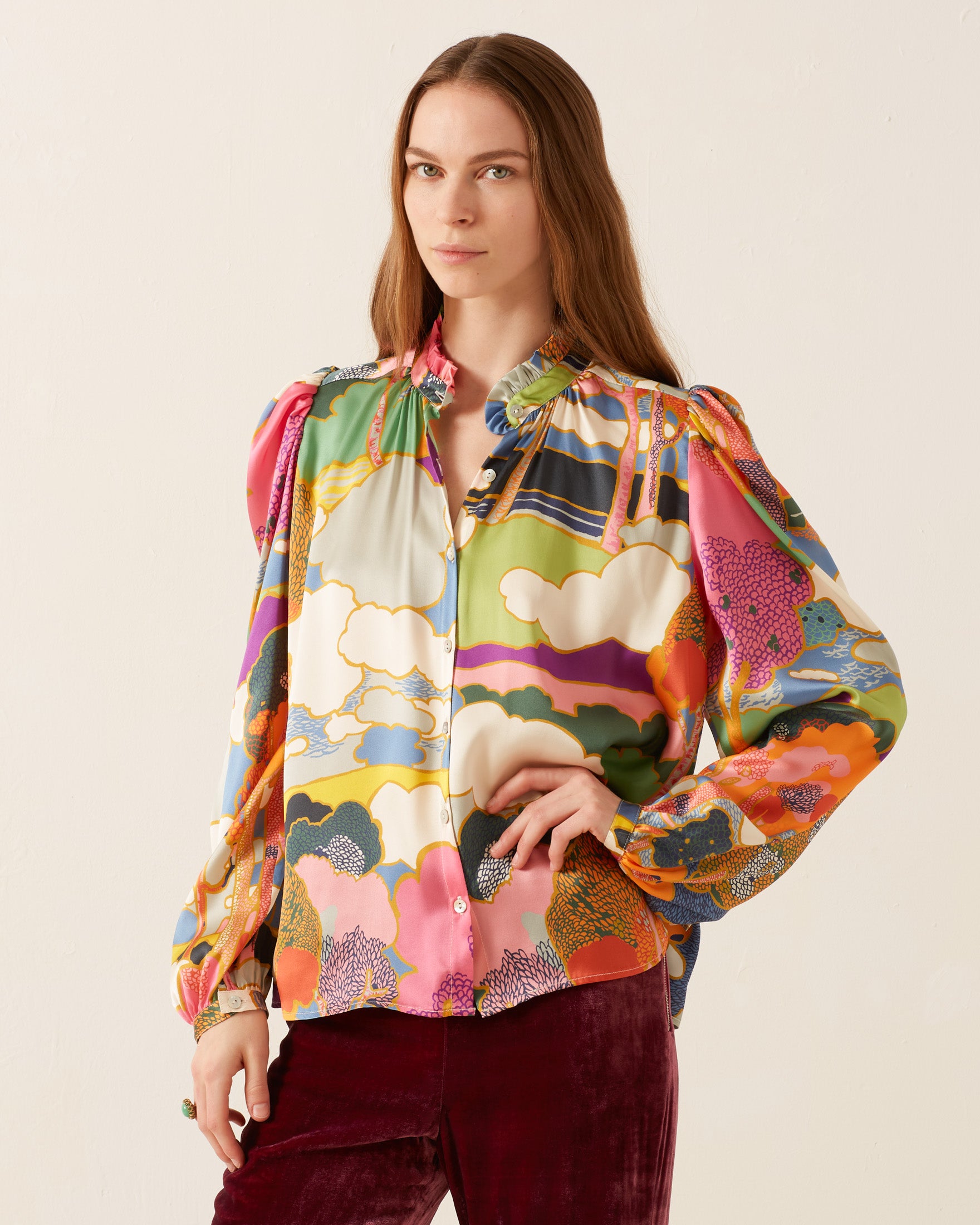 A person wearing the eye-catching Annabel Aurora Silk Shirt, featuring a vibrant Liberty print, and red velvet pants stands against a plain background.