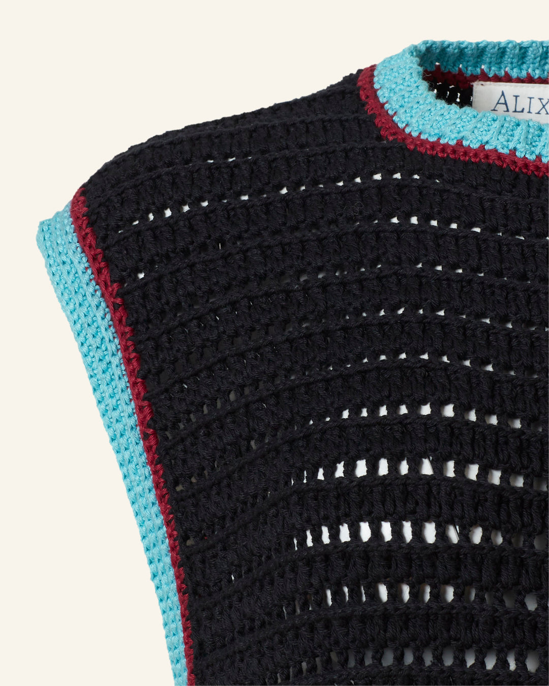 Close-up of the Omer Equinox Crochet Top, a vintage-inspired black knit with blue and red trim along the neckline and armholes; a small clothing label is partly visible.