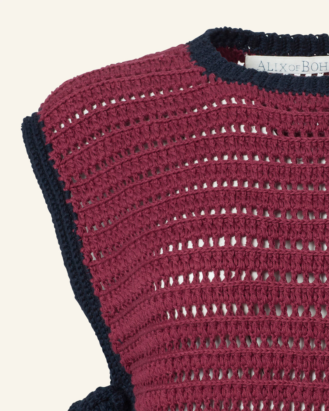 Close-up of the Oona Mulberry Crochet Top, a vintage-inspired maroon cropped piece with navy trim and textured open weave. "ALIX OF BOH" label is partially visible at the neckline of this hand-crocheted design.