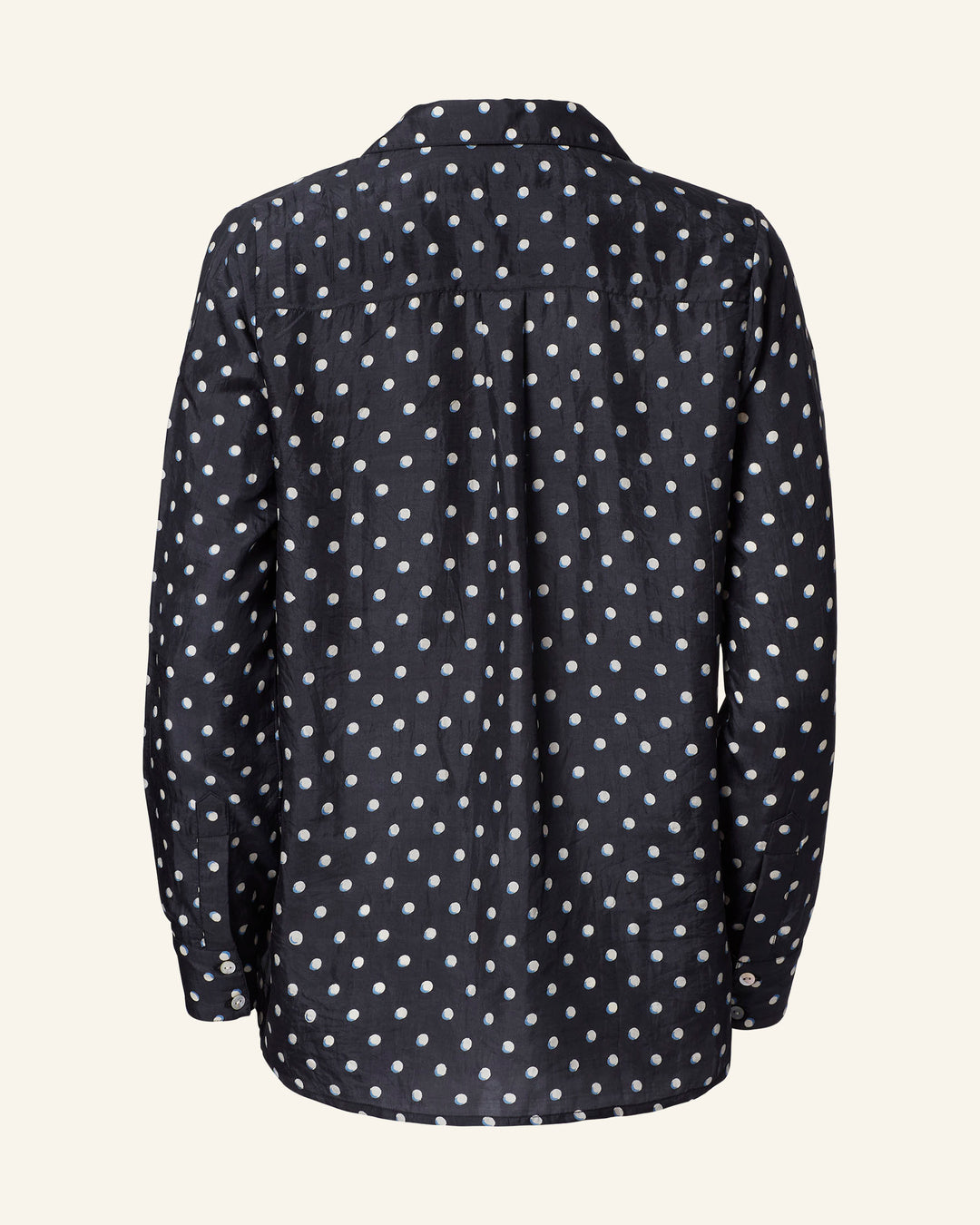 The Patti Raven Dot Silk Shirt showcases a back view with white dots on a black background. Its pajama-style cut contributes to a relaxed vibe, complete with a collar and buttoned cuffs.