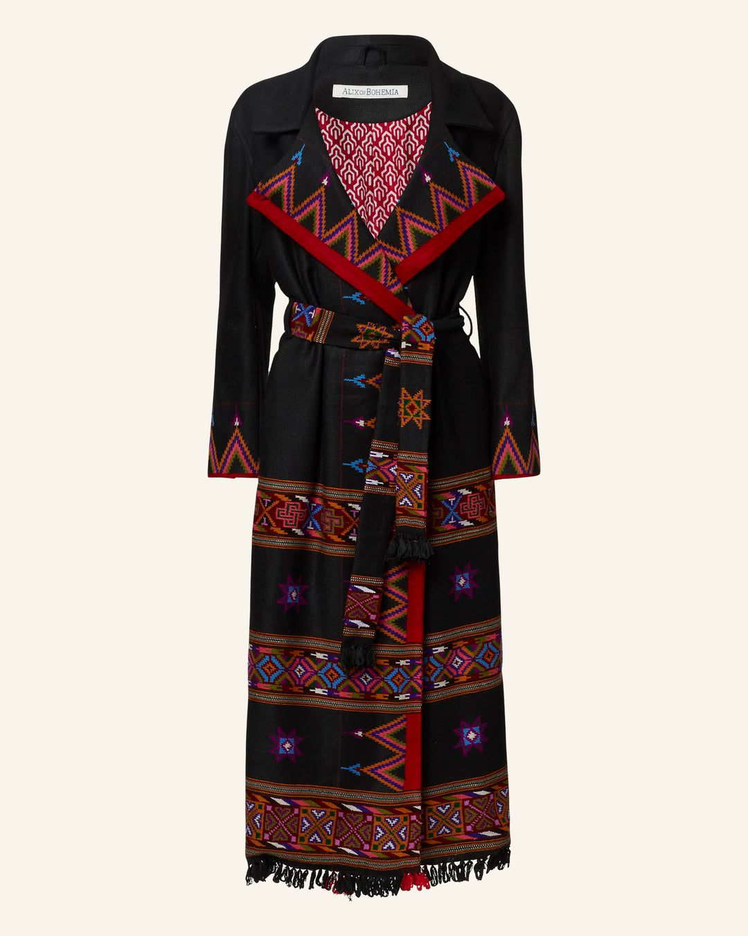 The Penelope Wildflower Wool Coat is a long black coat crafted from wool, featuring vibrant red, purple, and orange embroidered geometric patterns. This handcrafted garment boasts a wide lapel, a belt at the waist, and a patterned red and white lining. The fringe detailing along the hem adds a Western-inspired touch of flair.