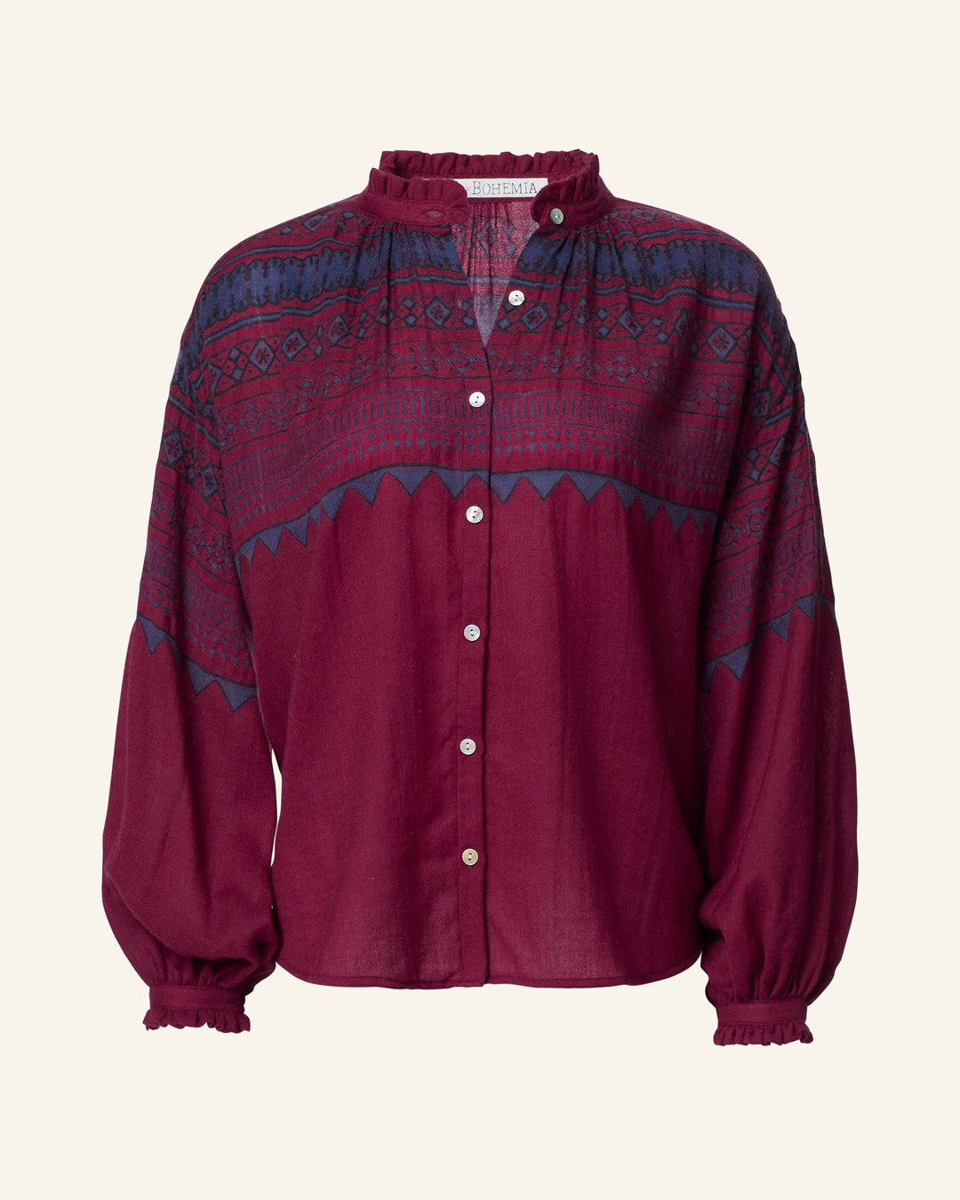 The Poet Plum Fairisle Blouse is a maroon hand-block printed button-up top adorned with a blue geometric pattern and features ruffled collar and cuffs.