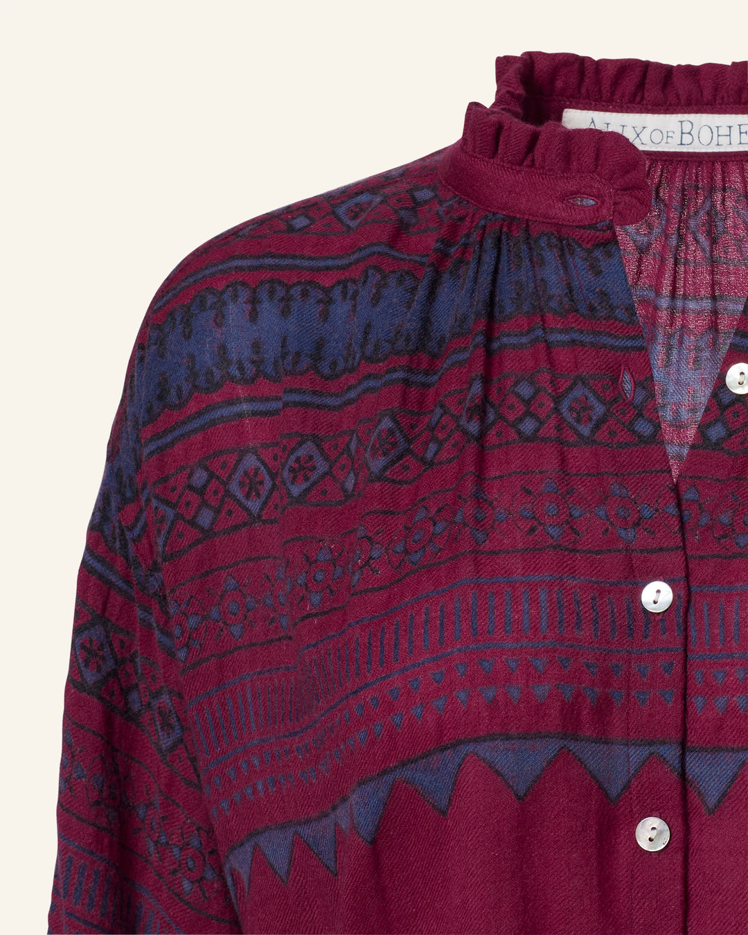 A close-up of the Poet Plum Fairisle Blouse, a vintage-inspired piece with a maroon and navy pattern, featuring a ruffled collar and white buttons.