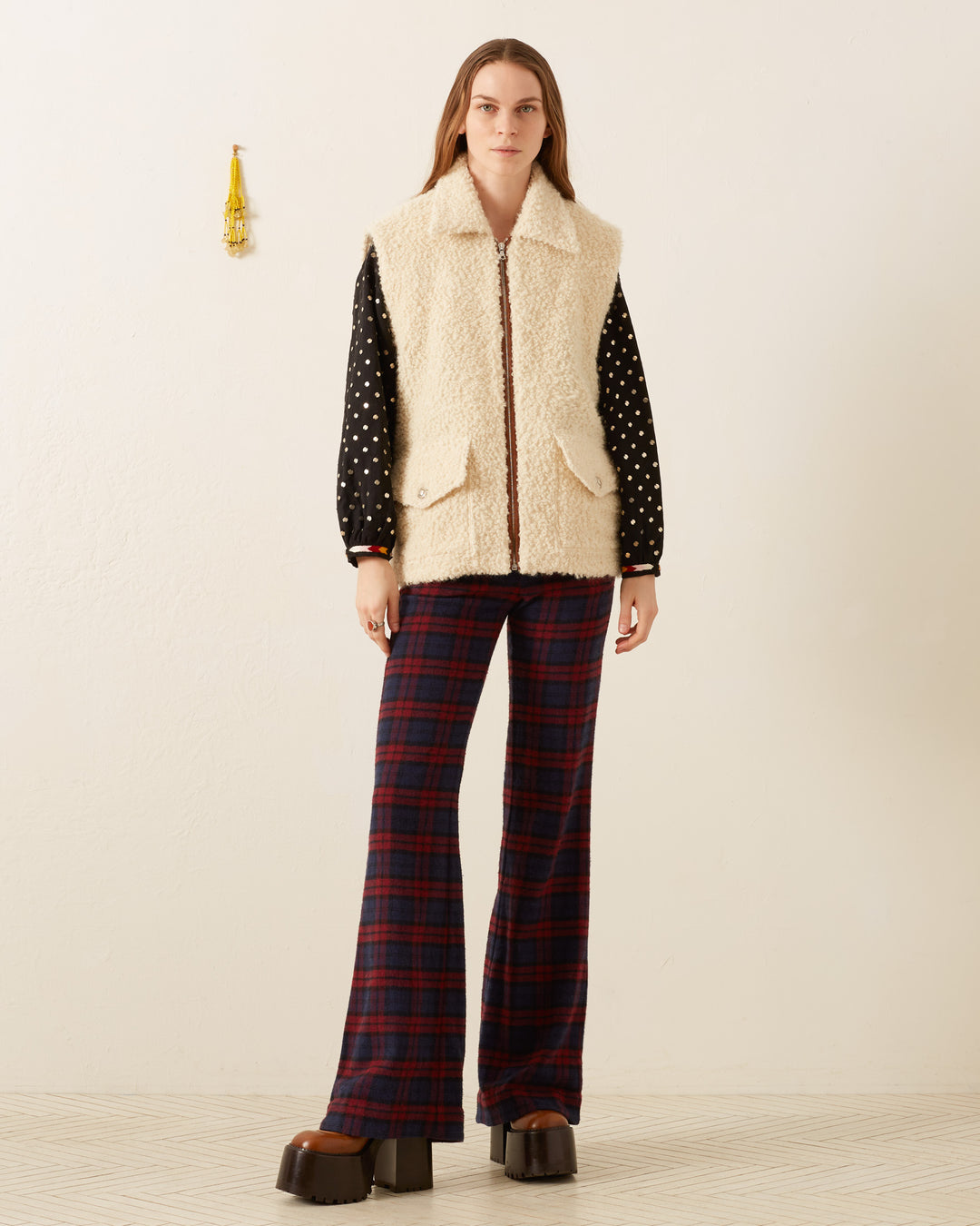 A person stands in a neutral-toned room, wearing the Mickey Suri Wool Vest over a black polka dot shirt and plaid trousers, perfect for winter layering.