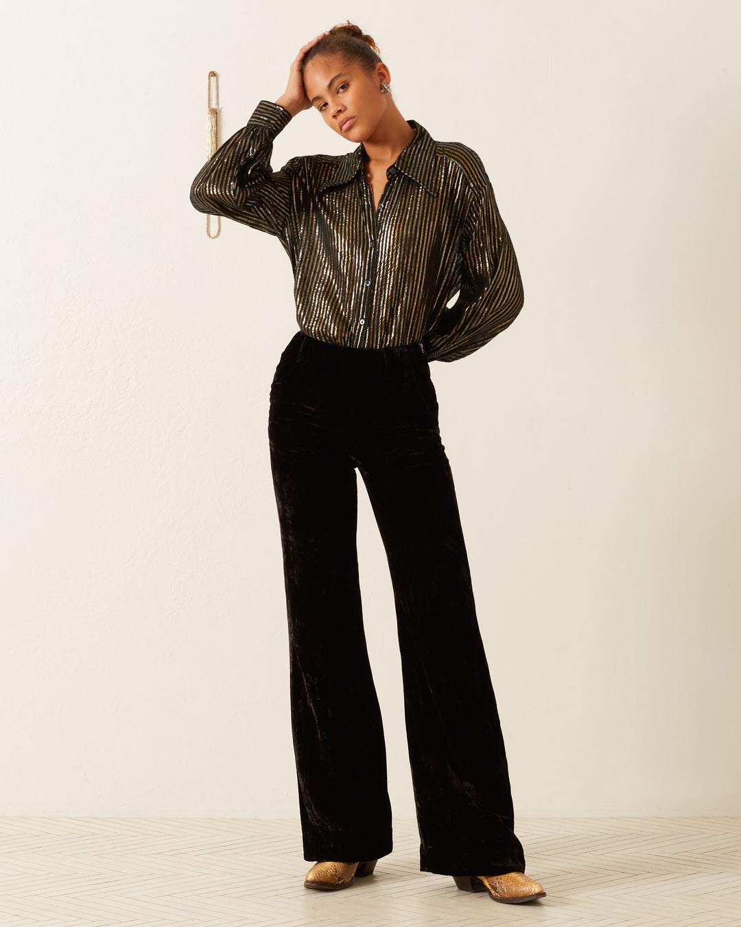 A person wears the Emery Moonlight Shirt, characterized by its metallic stripes and '70s-style wing collar, paired elegantly with black velvet pants and gold shoes, standing against a plain background.