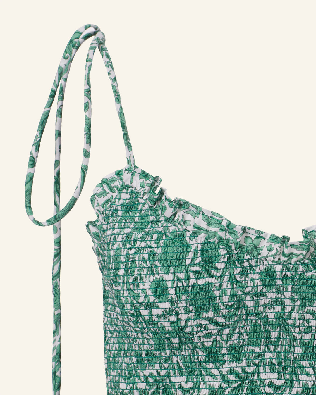 The Clara Laurel Vine Top features a close-up of green and white Liberty-print fabric with a smocked texture, a ruffled neckline, and slender shoulder straps, offering an effortlessly chic vibe.