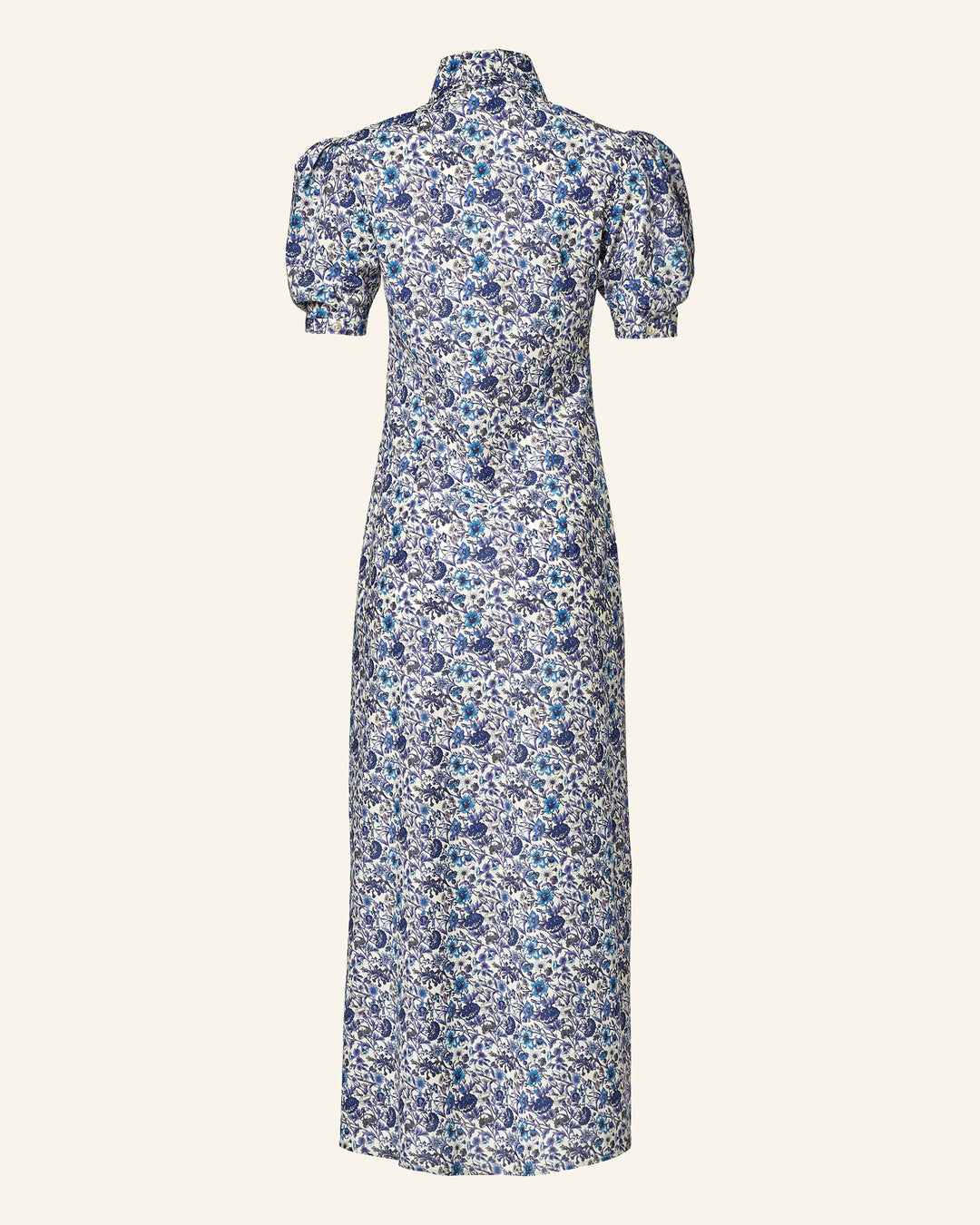 The Deneuve Luna Flower Dress is a long, high-collared piece with short puffed sleeves and a fitted silhouette, adorned in a blue and white Liberty floral print. Made from Italian cotton lawn, it stands out against a plain background.