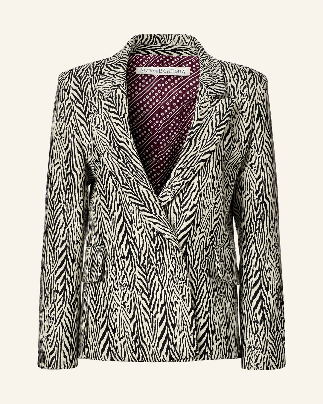 The Dree Zebra Blazer, crafted from virgin wool, features a striking black-and-white zebra stripe pattern. It is elegant with a peak lapel and has a maroon and white paisley lining for added style.